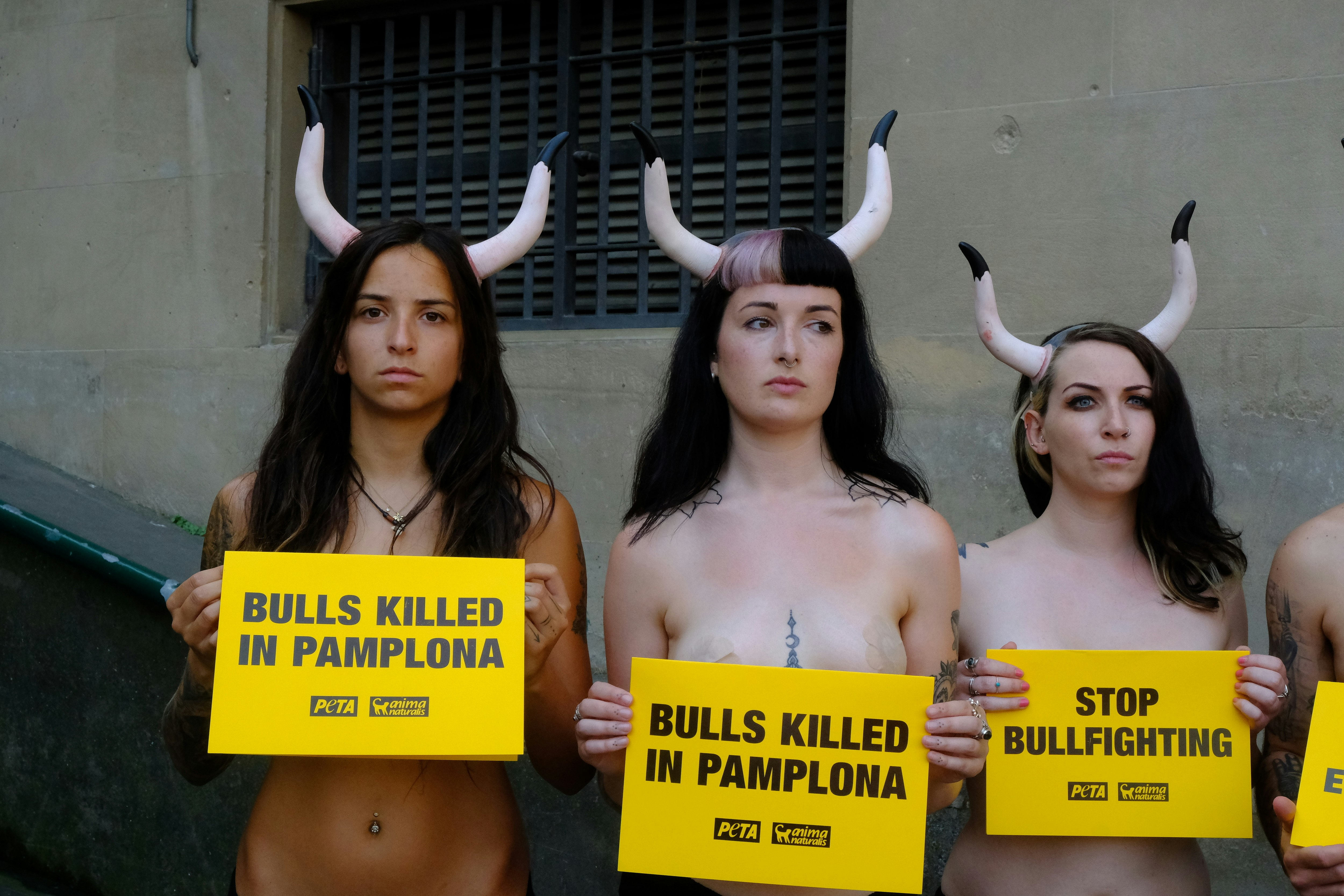 A trio of topless woman wearing bull horns hold signs over their chests that call for the end of bullfighting  