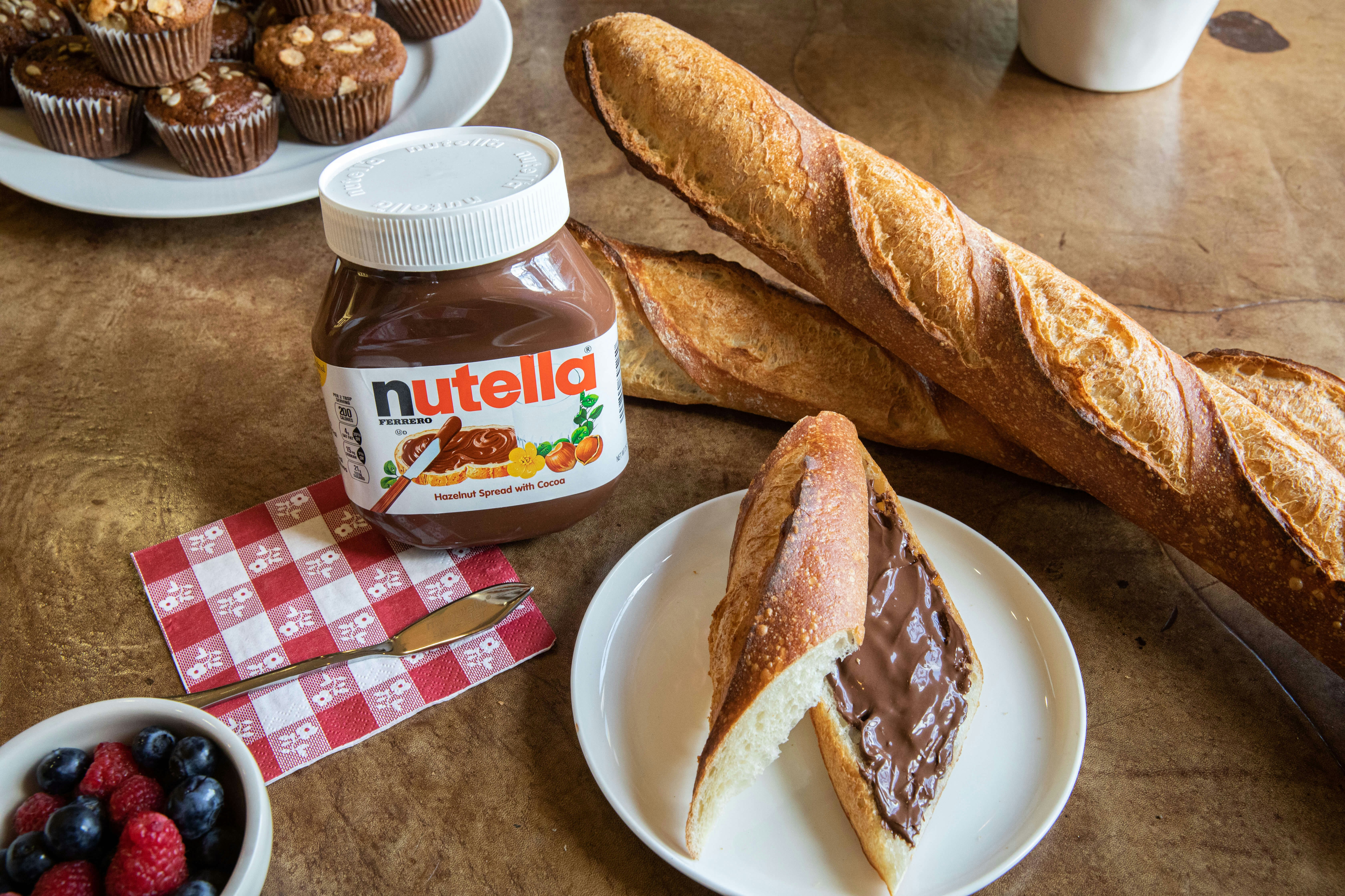 A table with a jar of Nutella, two baguettes, and slices of bread with Nutella 
