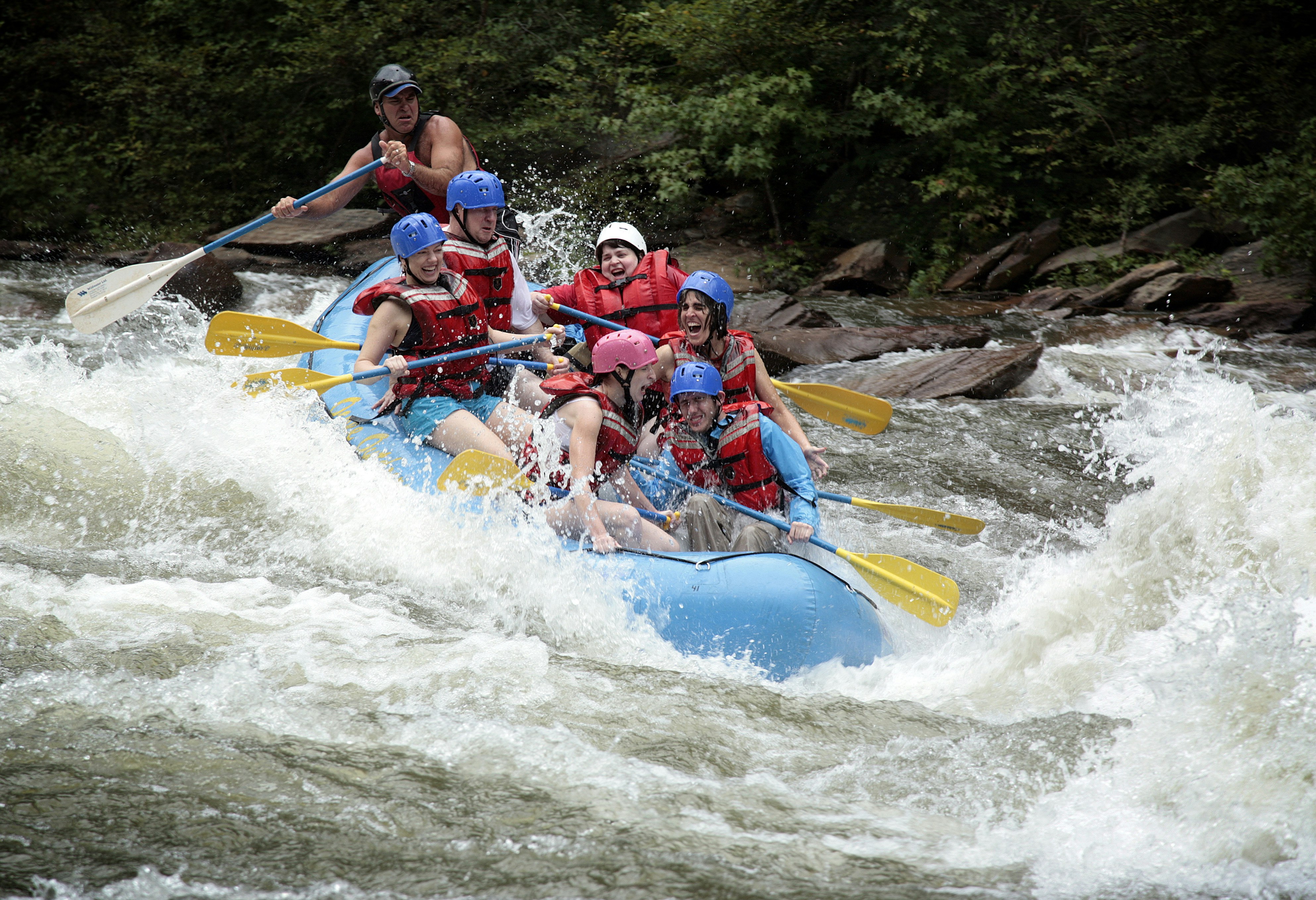 A group of people wearing helmets and life jackets smile as they white-water raft at the Ocoee Whitewater Center