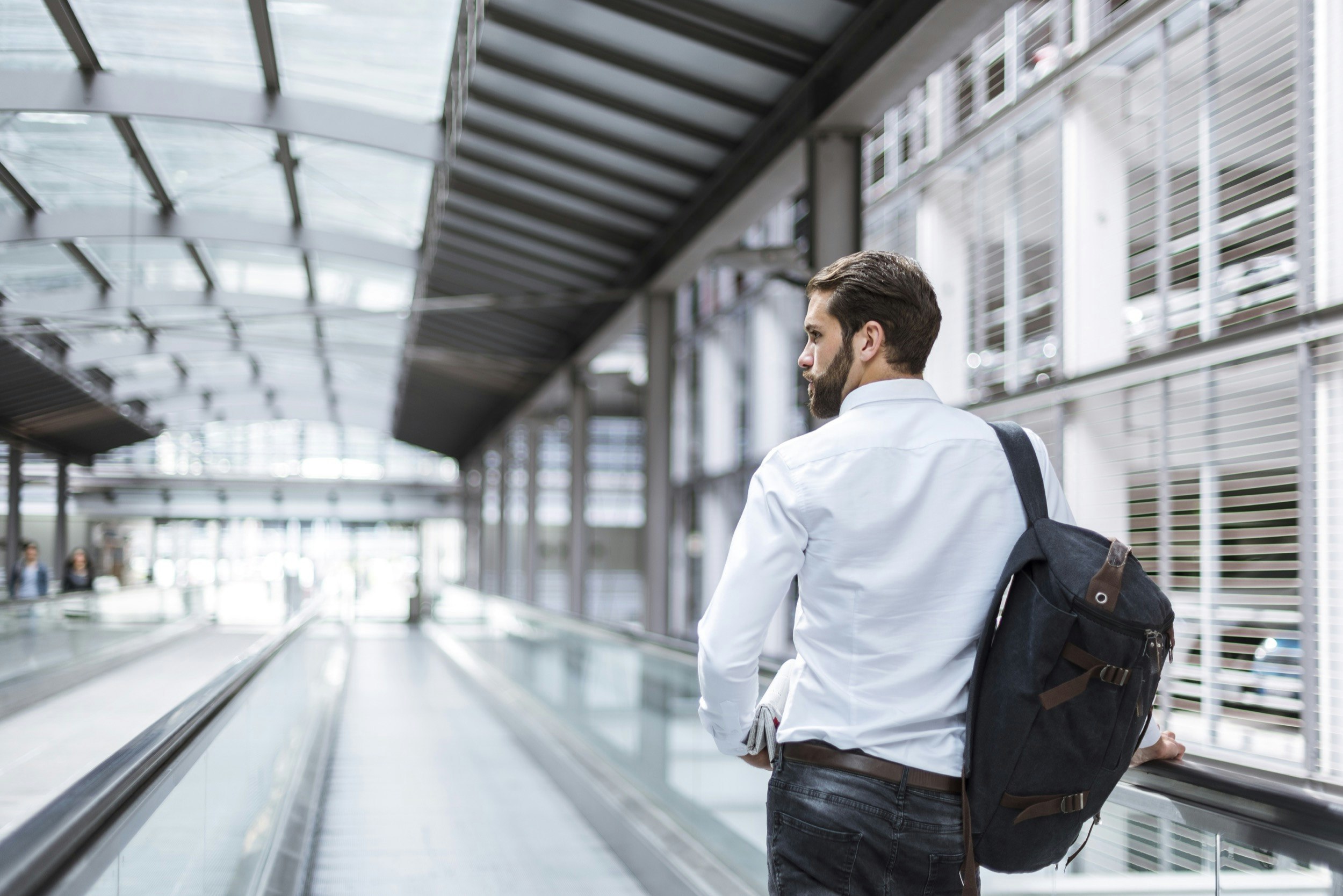 A man rides a moving walkway in an airport while carrying a duffle bag over his shoulder; Upgrade your travel game