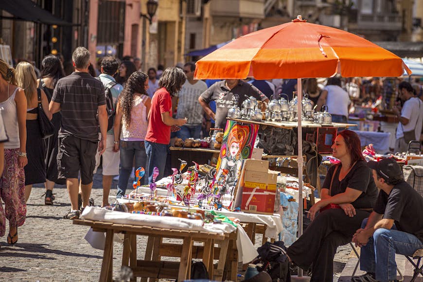 A woman sits under an orange umbrella at an art stall at San Telmo Market, Buenos Aires