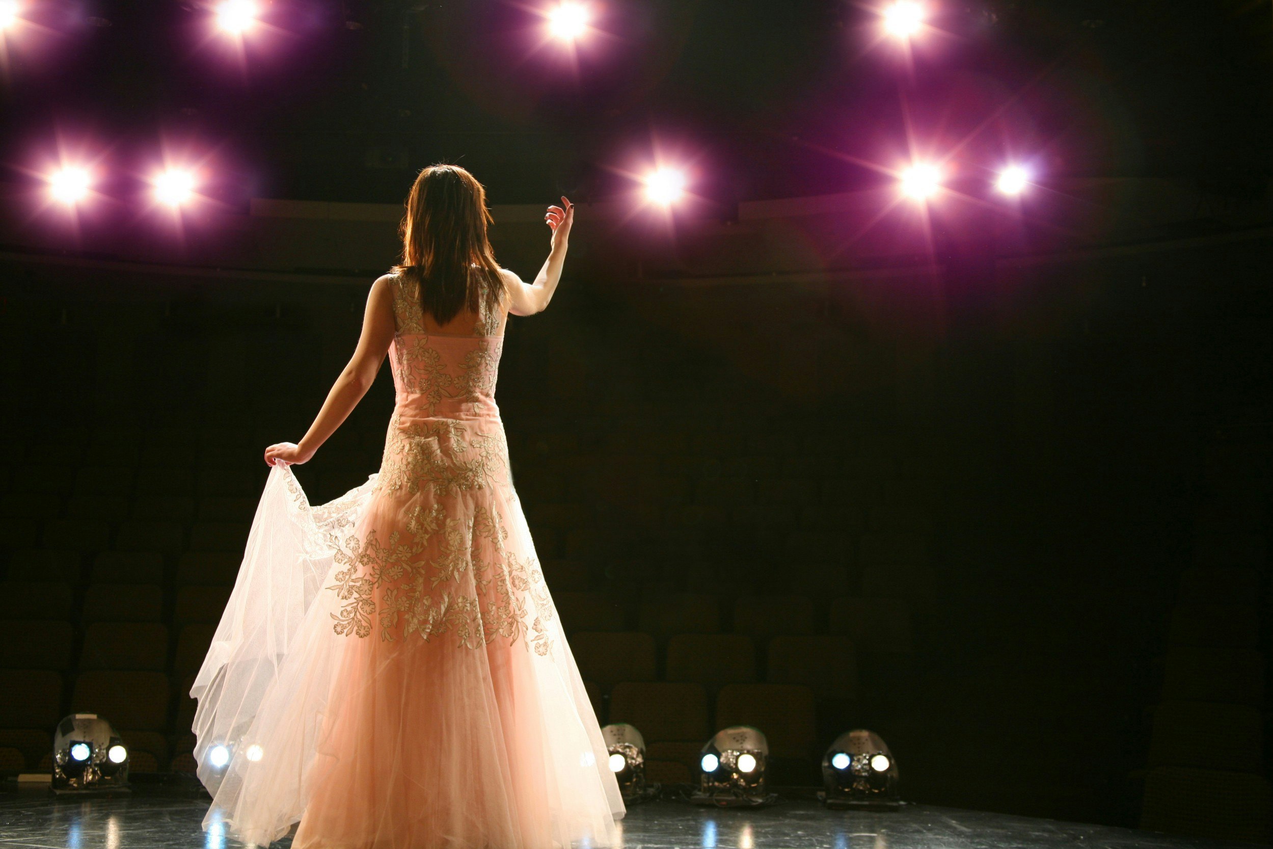 A female opera singer on a stage singing to an empty auditorium