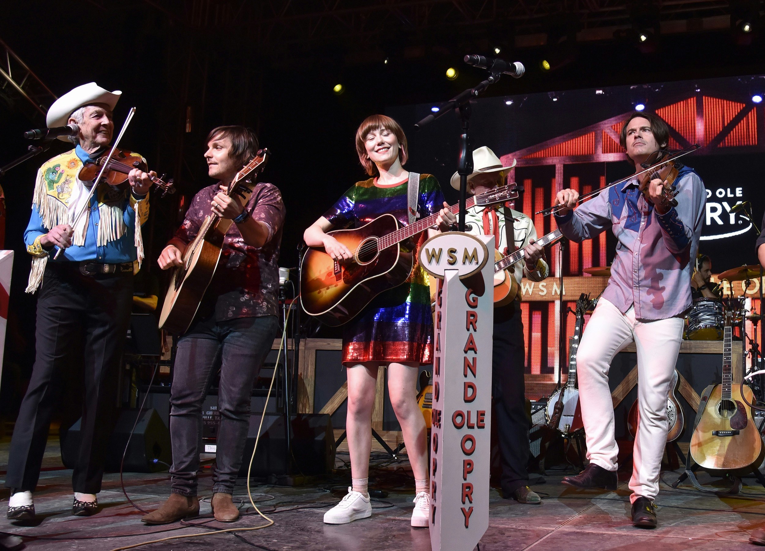 A diverse collection of country music artists gather around the microphones on stage at the grand ole opry in Nashville; Best places for country music in Nashville