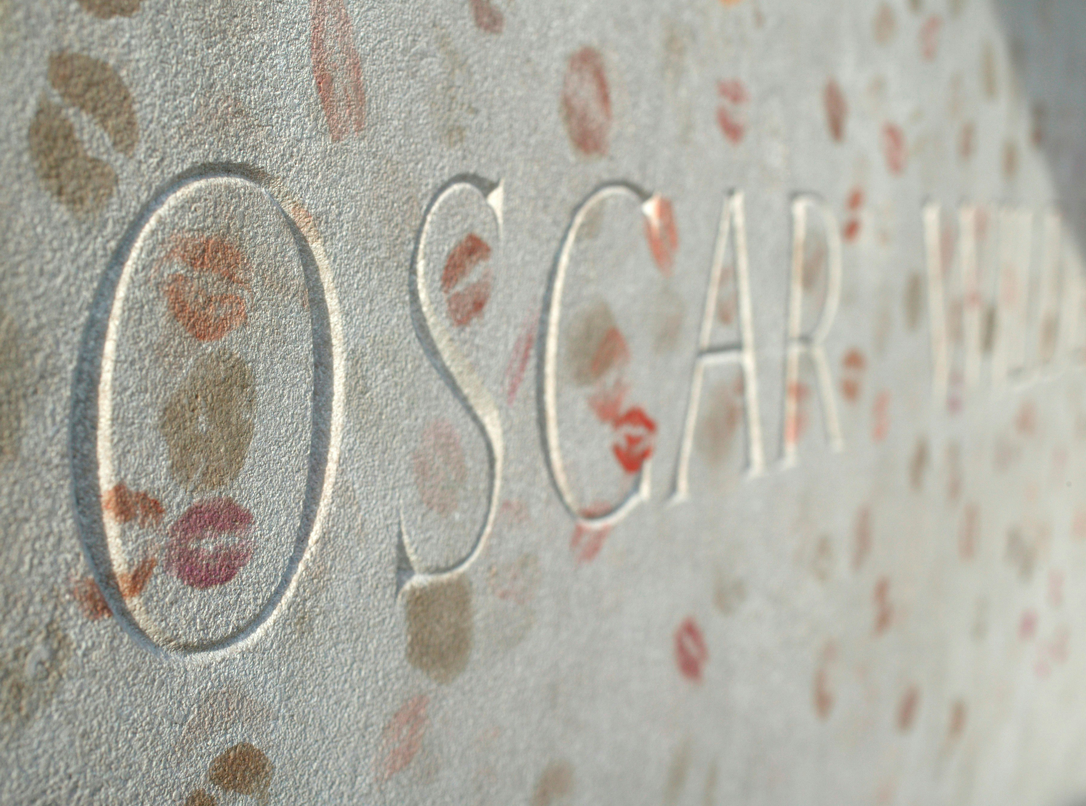 A close-up of the words 'Oscar Wilde' taken from the poet's tomb in Paris. The tomb is covered in lipstick kiss marks from visitors.