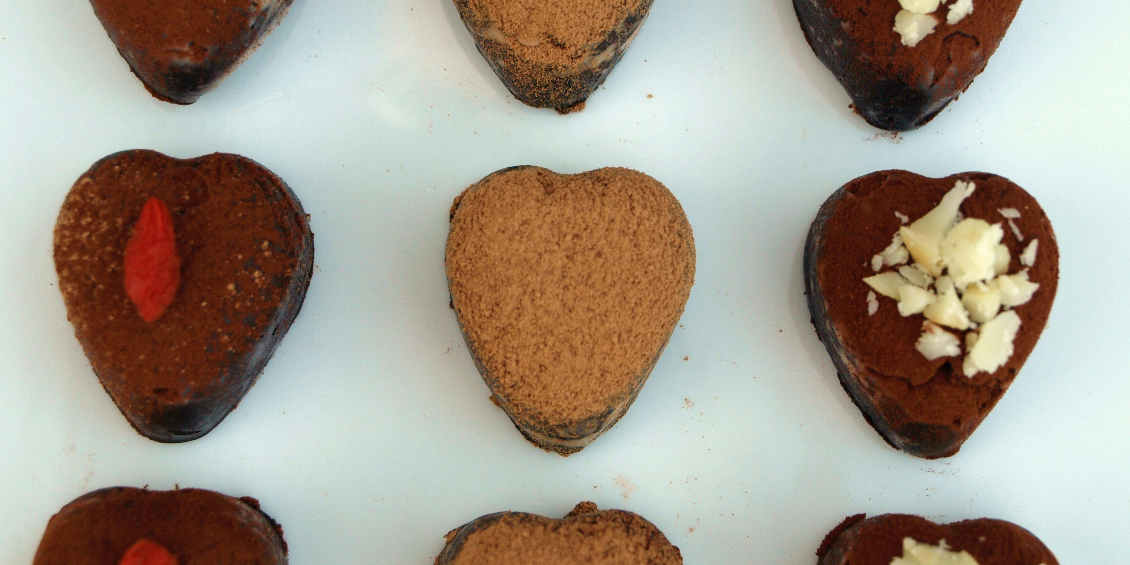 Heart-shaped chocolate deserts are laid out neatly in rows. Some are topped with chopped nutes, and others with a piece of raspberry.