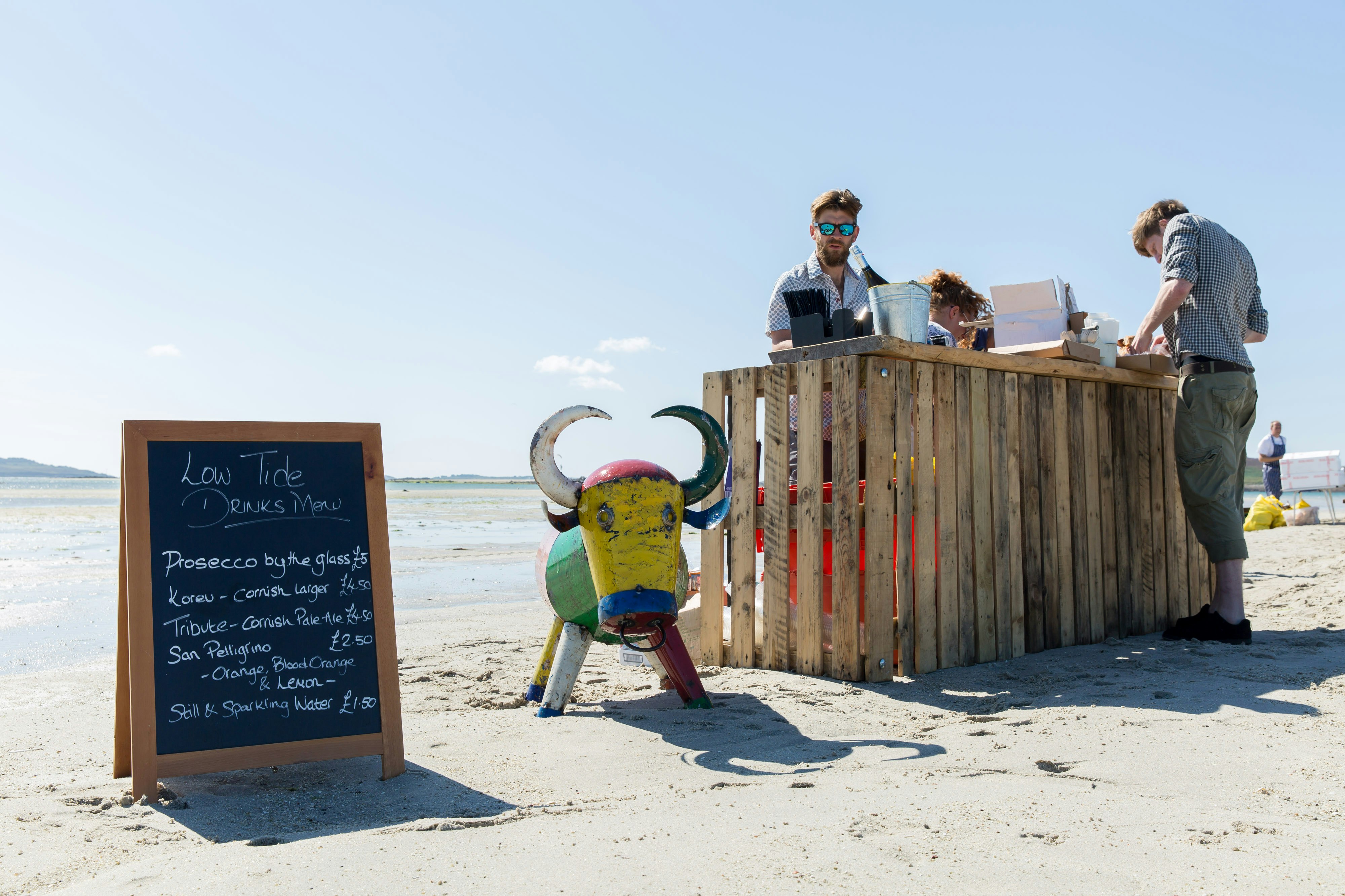People serve drinks from a kiosk on a sand bar during low tide. 