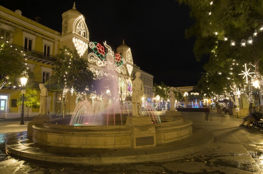 Water in a fountain is light up in red and green colors on a highly decorated plaza for Christmas in Puerto Rico