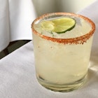 Closeup of a chilli-salt rimmed glass of the Paloma cocktail made with tequila and grapefruit juice. There is a lime slice in the middle of the drink.