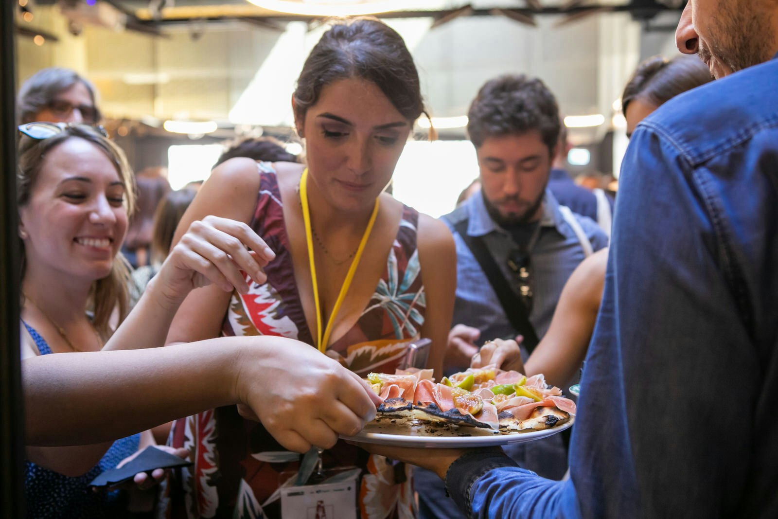 A woman looking down at the plate of food she is holding, surrounded by people who are reaching to get some food from the plate