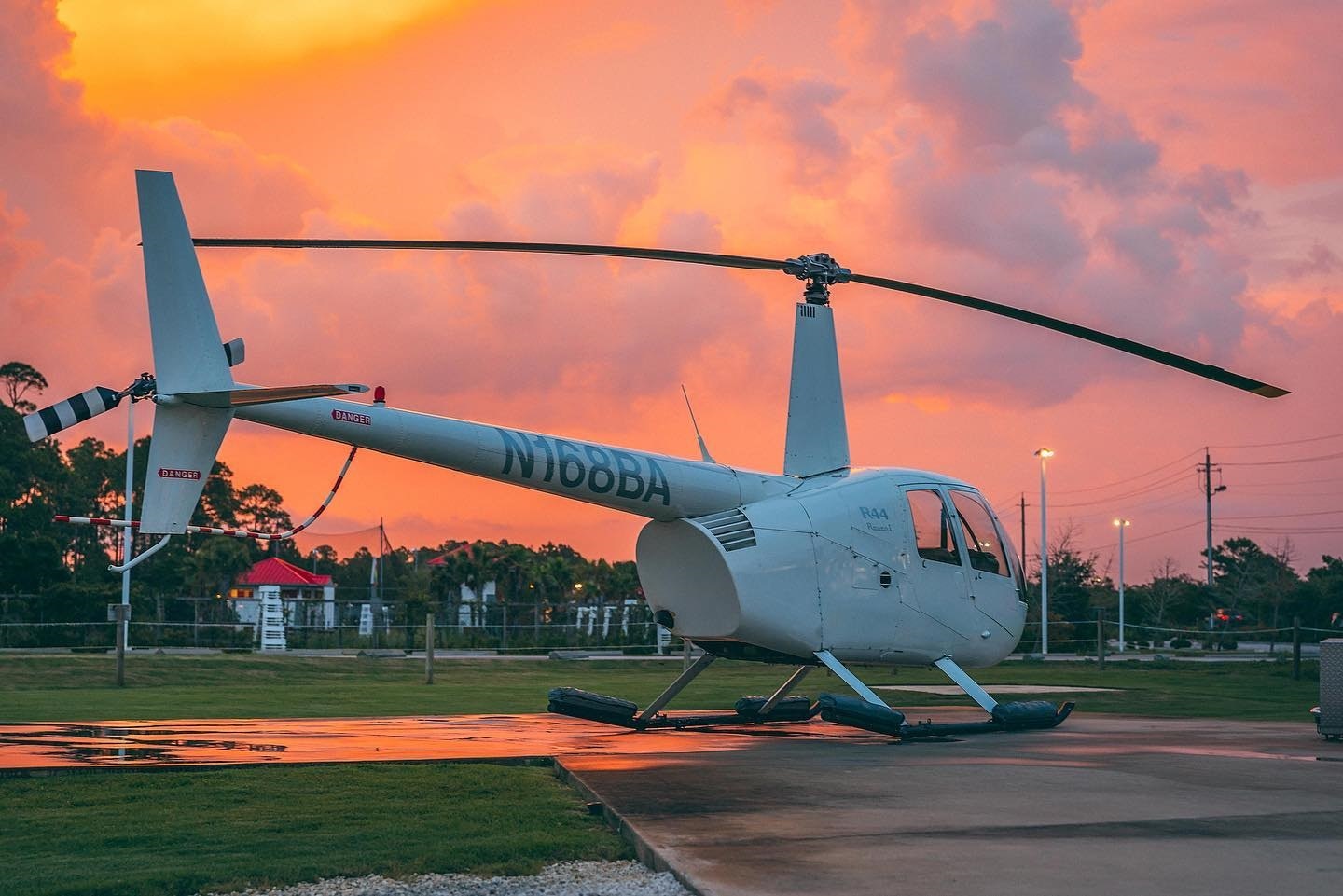A white helicopter sits on the ground ready to be boarded in front of a pink sunset sky