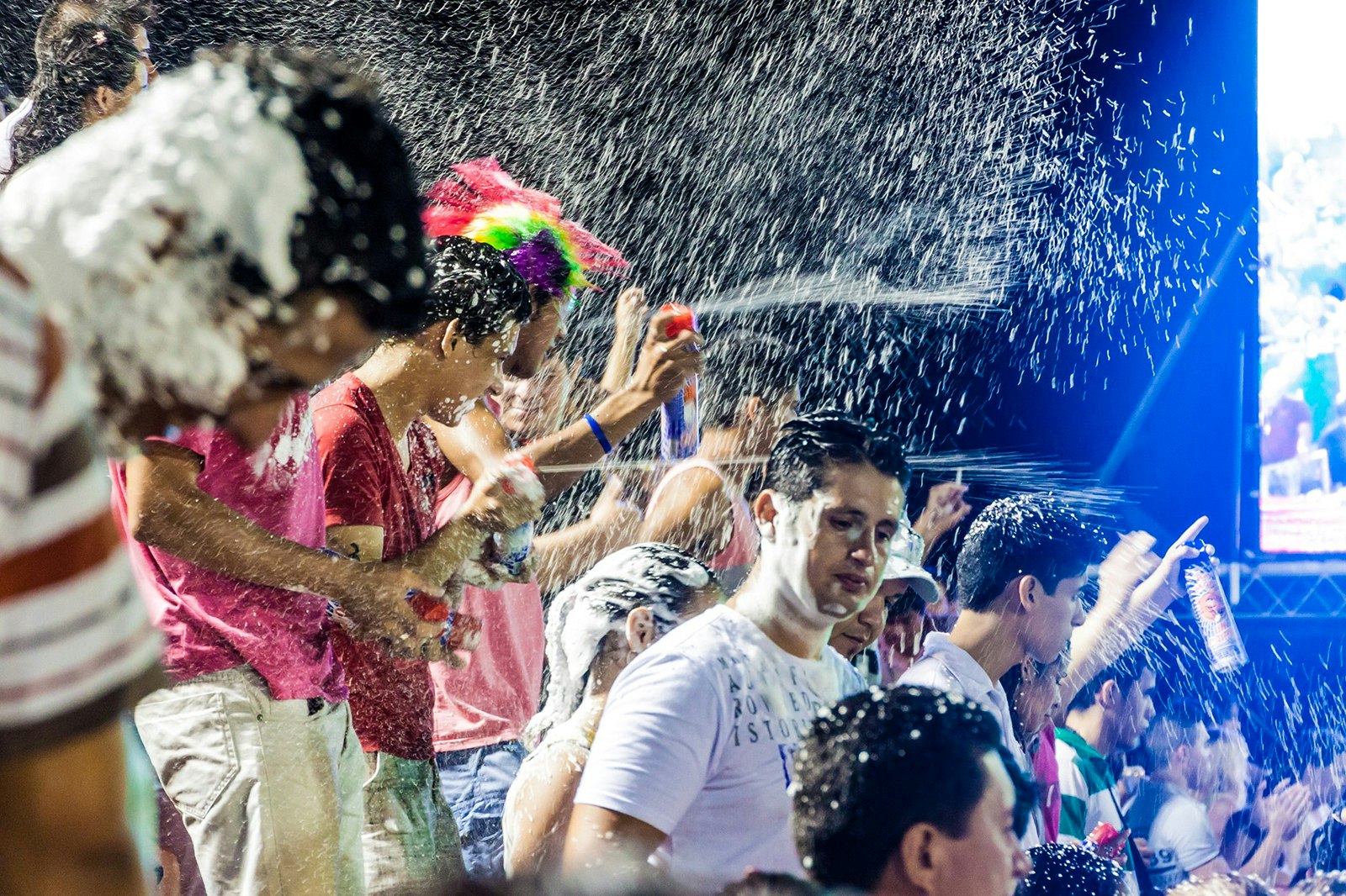 A group of people spray cans of fake snow in the air, covering those nearby 