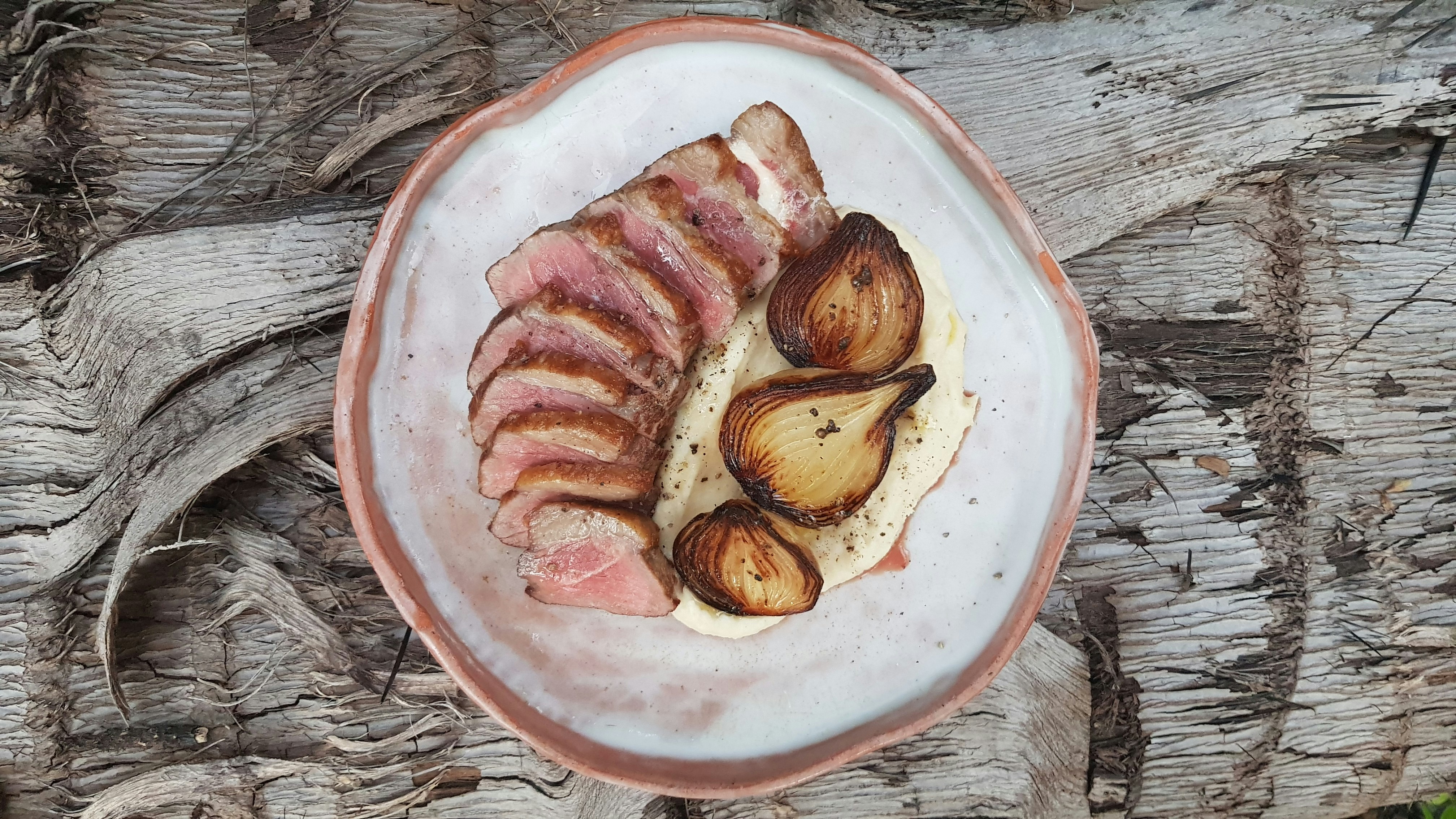 A close up of a plate of sliced meat with charred onion on a bed of white sauce