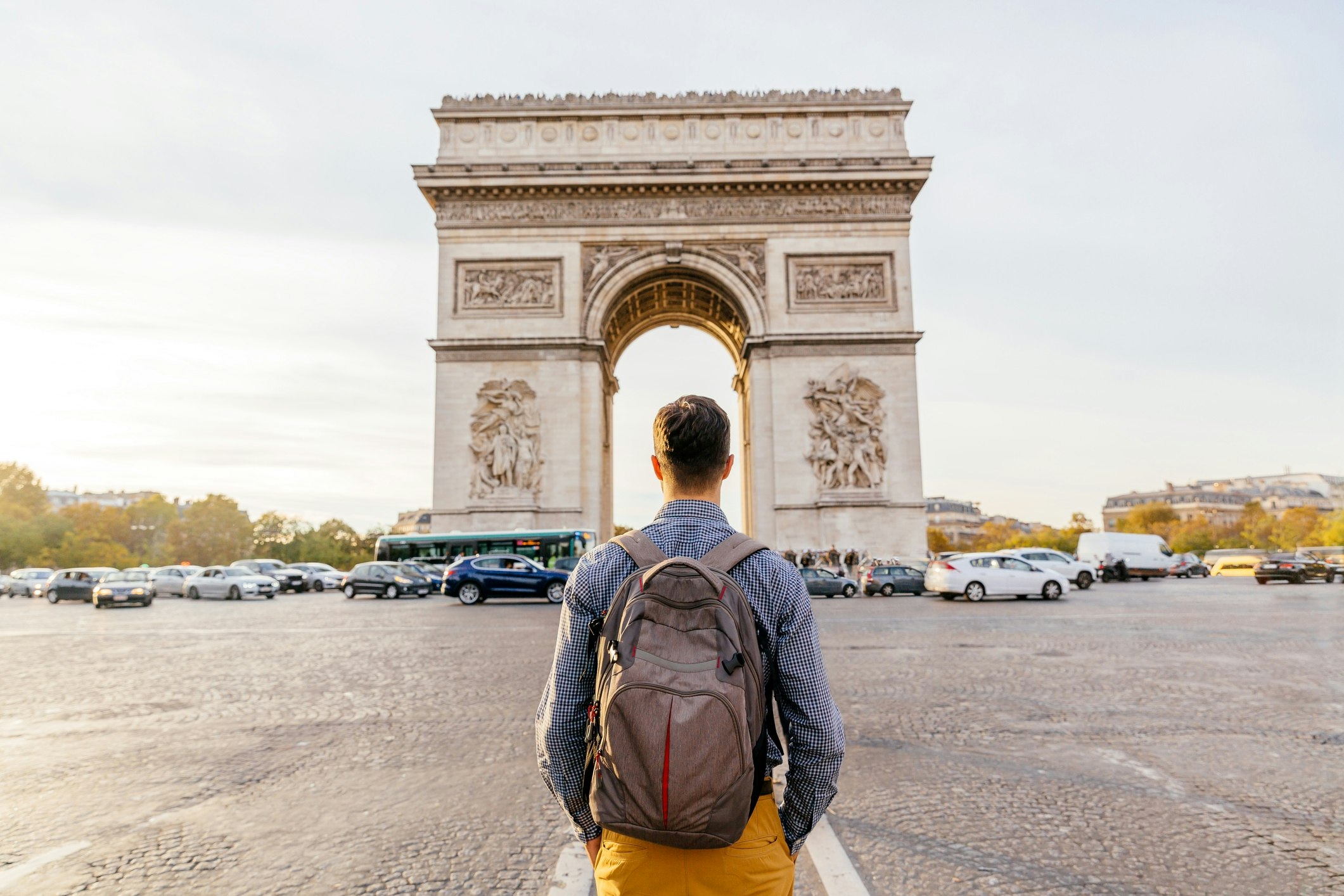 Man with a backpack standing in front of the Arc de Triomphe in Paris. 