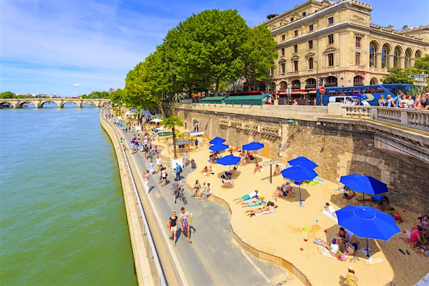 Paris Plages.jpg Sand lines one side of a walking path spiked with blue umbrellas along a river