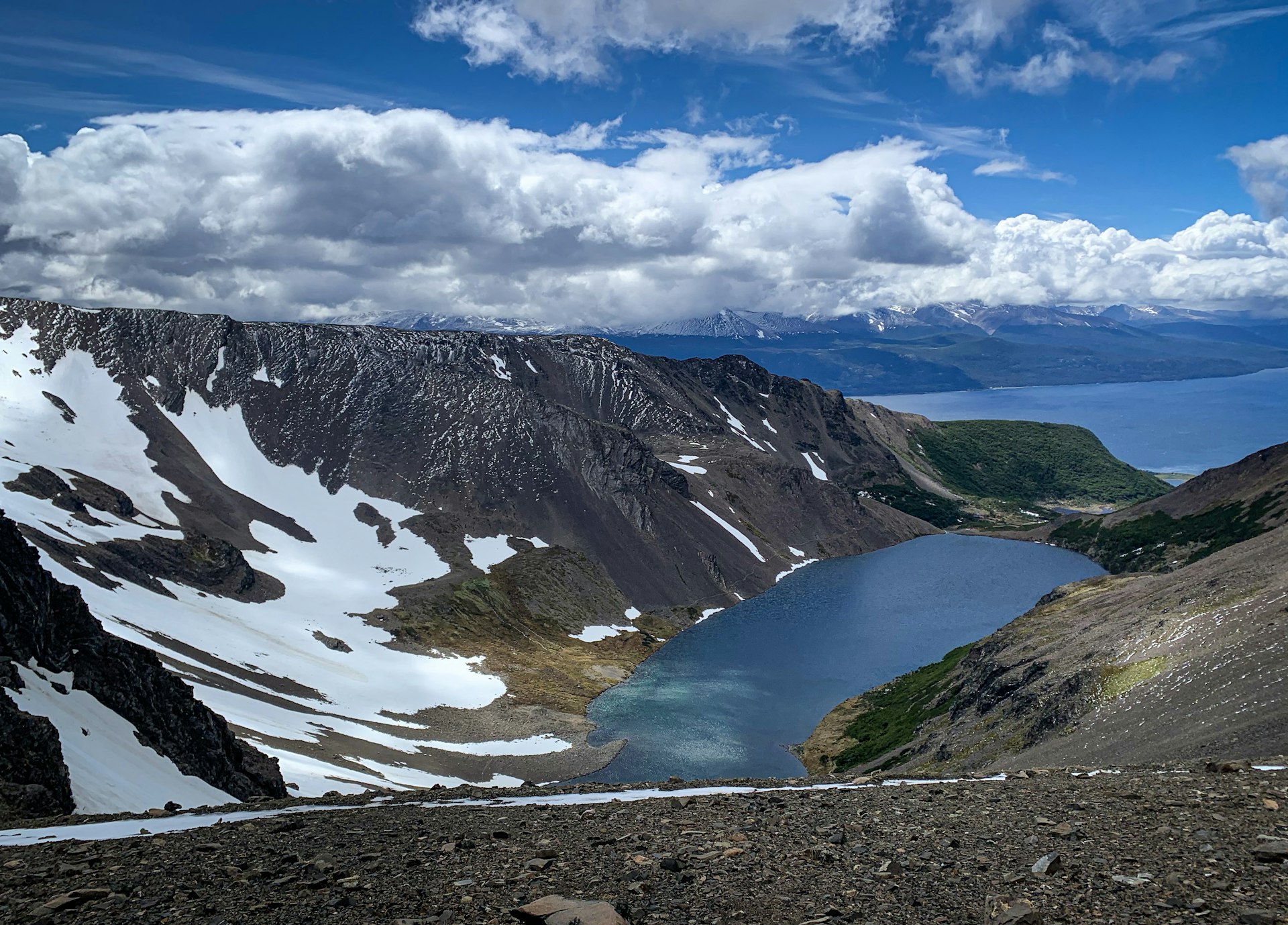 Looking down towards a lake at the bottom of an enormous 'bowl' surrounded by barren, snowy mountains.