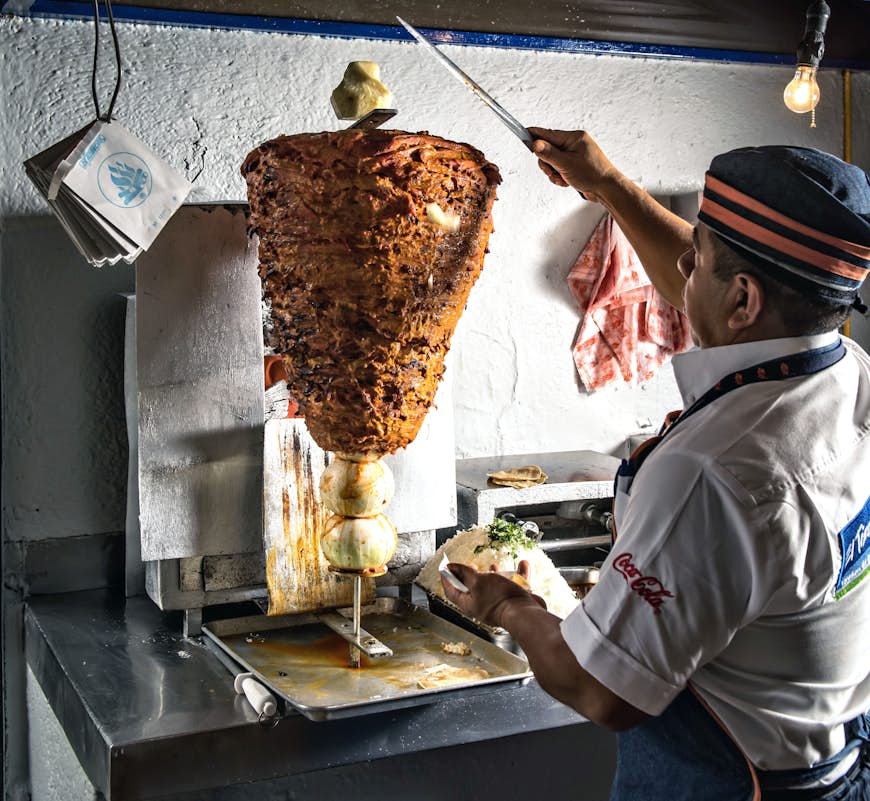 En man skär tunna skivor kött på en roterande metallstav på en restaurang i Mexico City