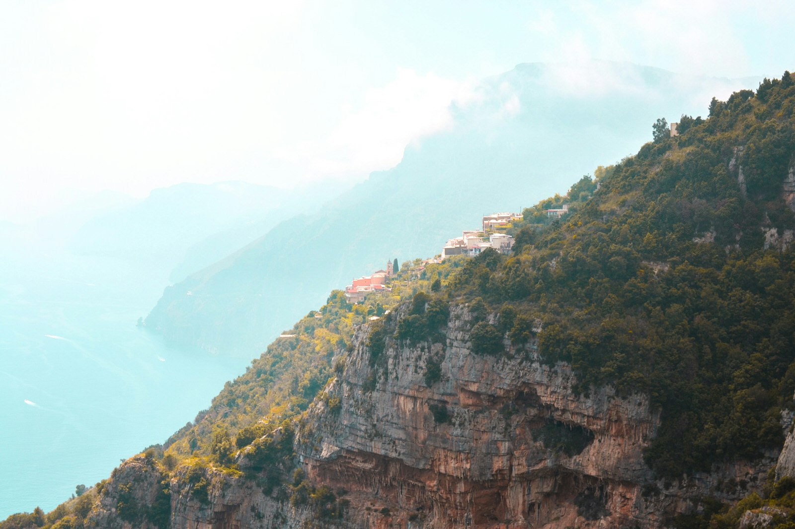 A photo of a hiking trail knows as Path of the Gods in Italy. Terracotta roofs are just about visible on the side of a forested mountain.