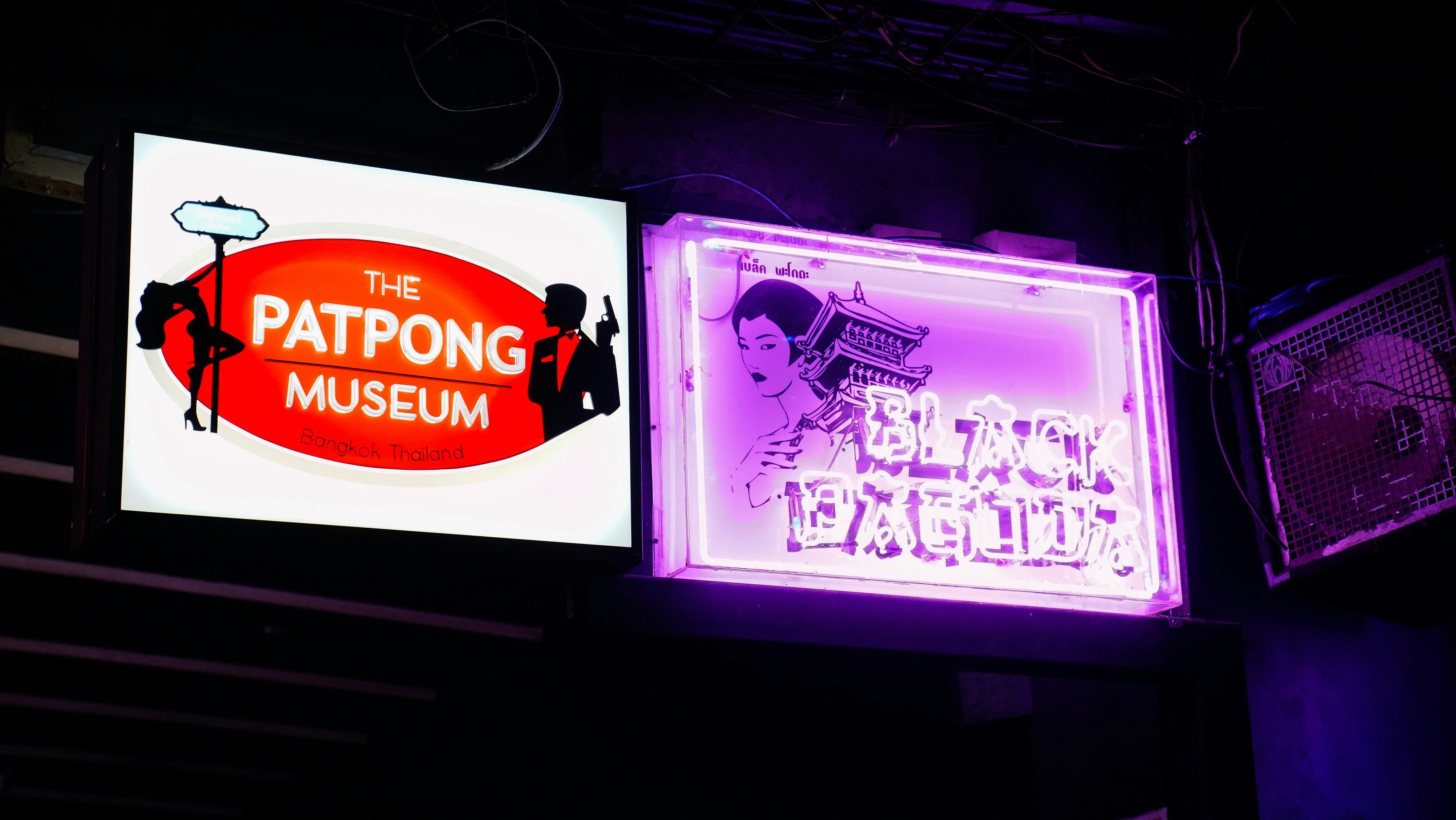 A view of the neon Patpong Museum sign, located on the street outside the museum. Next to it is a neon sign for the 'Black Pagoda'.