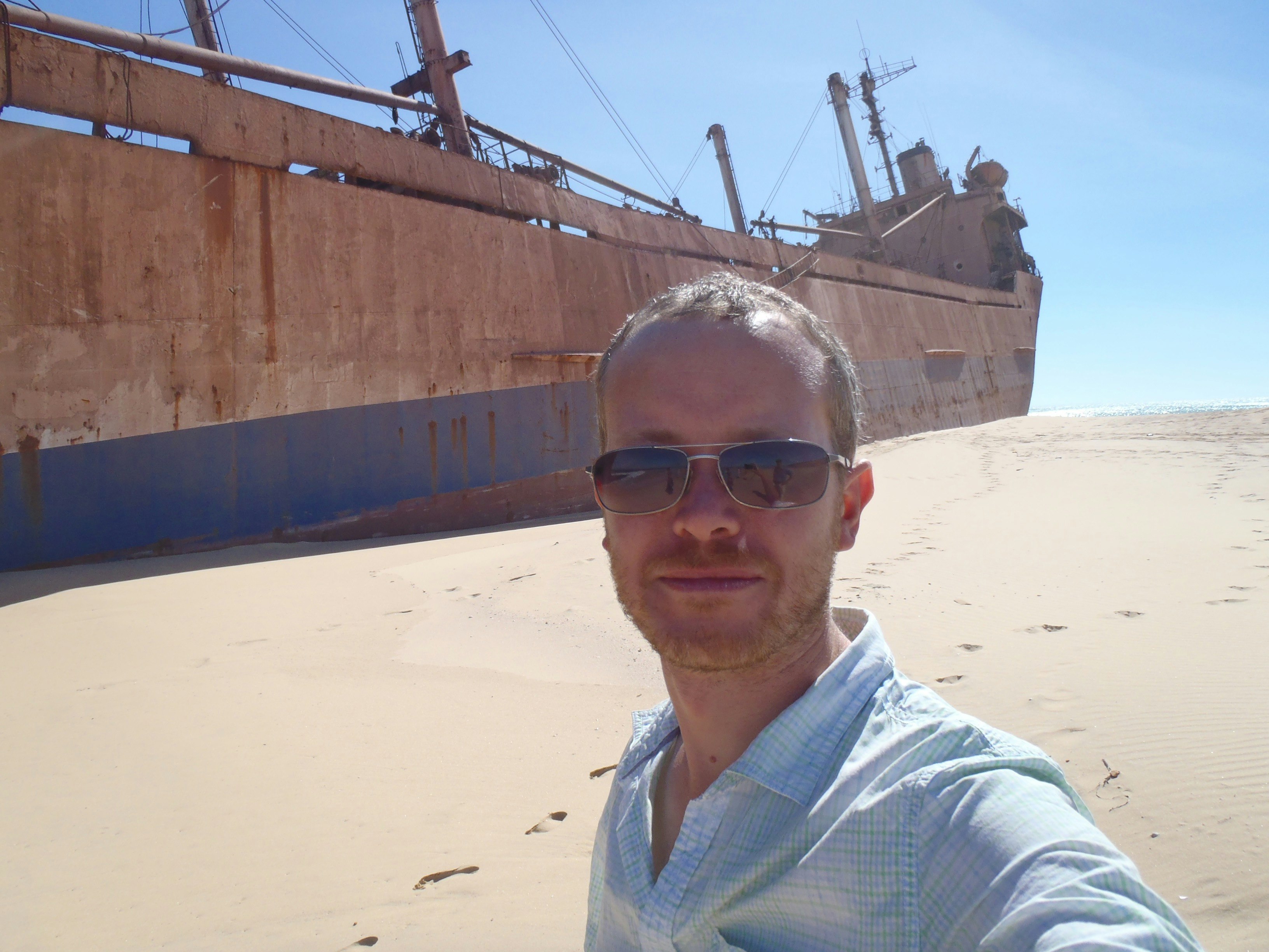Paul Clammer takes a selfie in front of an enormous shipwreck on a sandy beach in Mauritania.