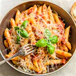 Pasta All'Arrabbiata, penne with tomato sauce and basil and parmesan cheese on a rustic wooden table with linen napkin