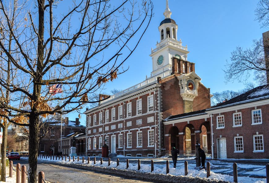 Snö täcker marken runt bladlösa träd i Independence Hall i Philadelphia