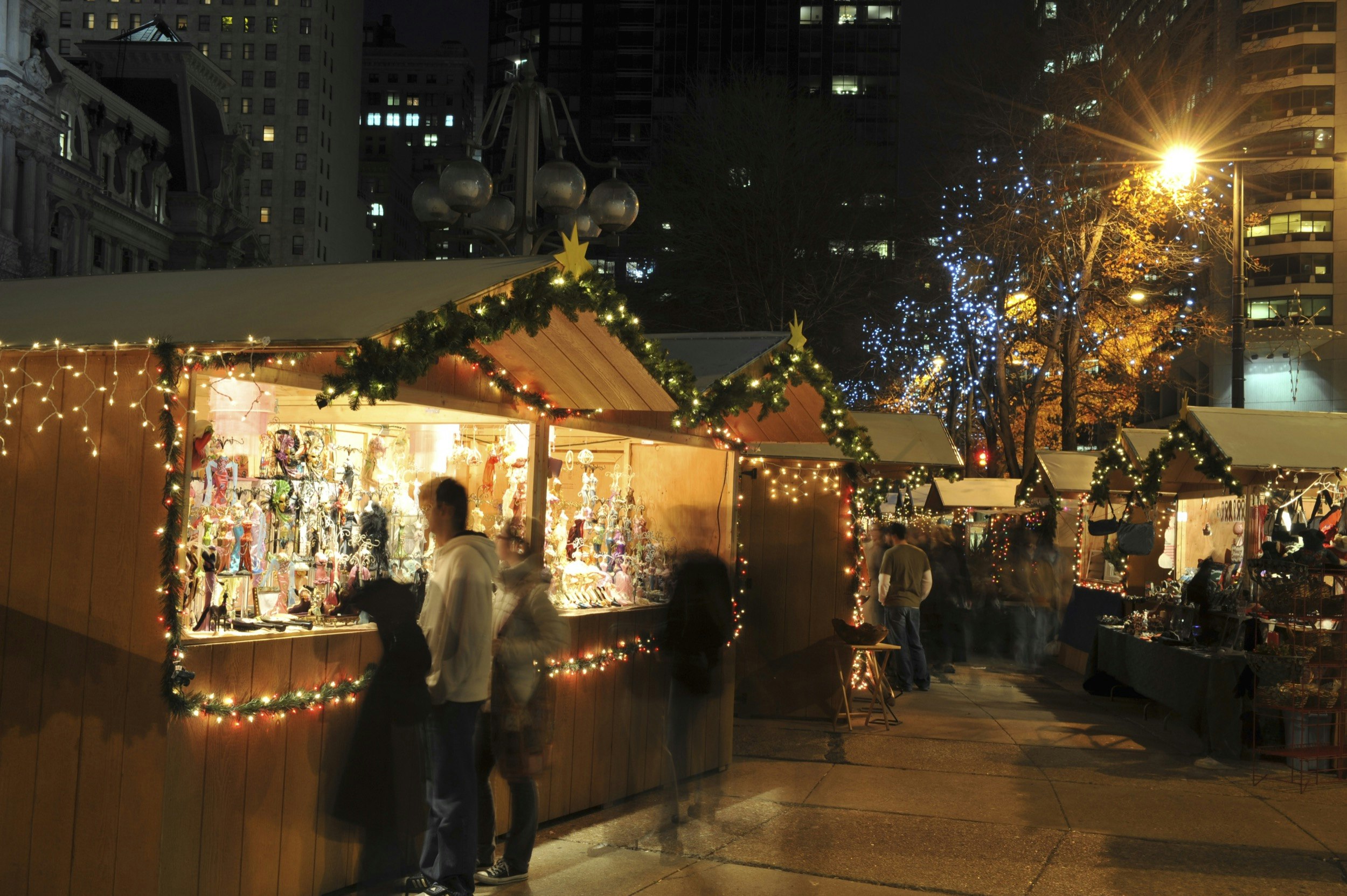 People walk past wooden merchant stalls during Christmas in Philadelphia at night