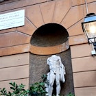A sign marks the home of Pablo Picasso, positioned on the building above and to the left of an alcove with a statue of a headless nude statue 
