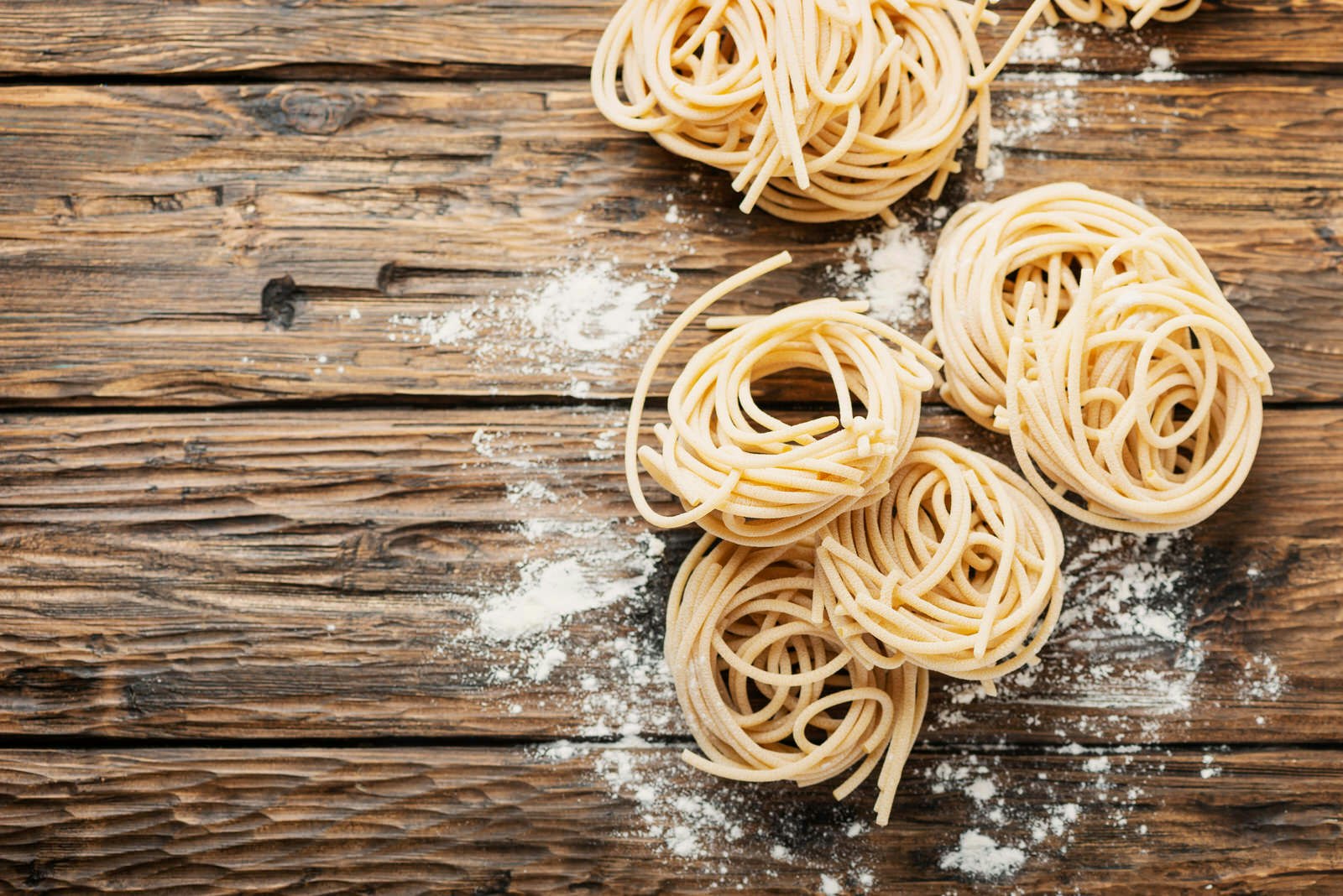 Flera okokta bollar av pici-pasta från Toscana på ett grovt träbord beströdd med mjöl.