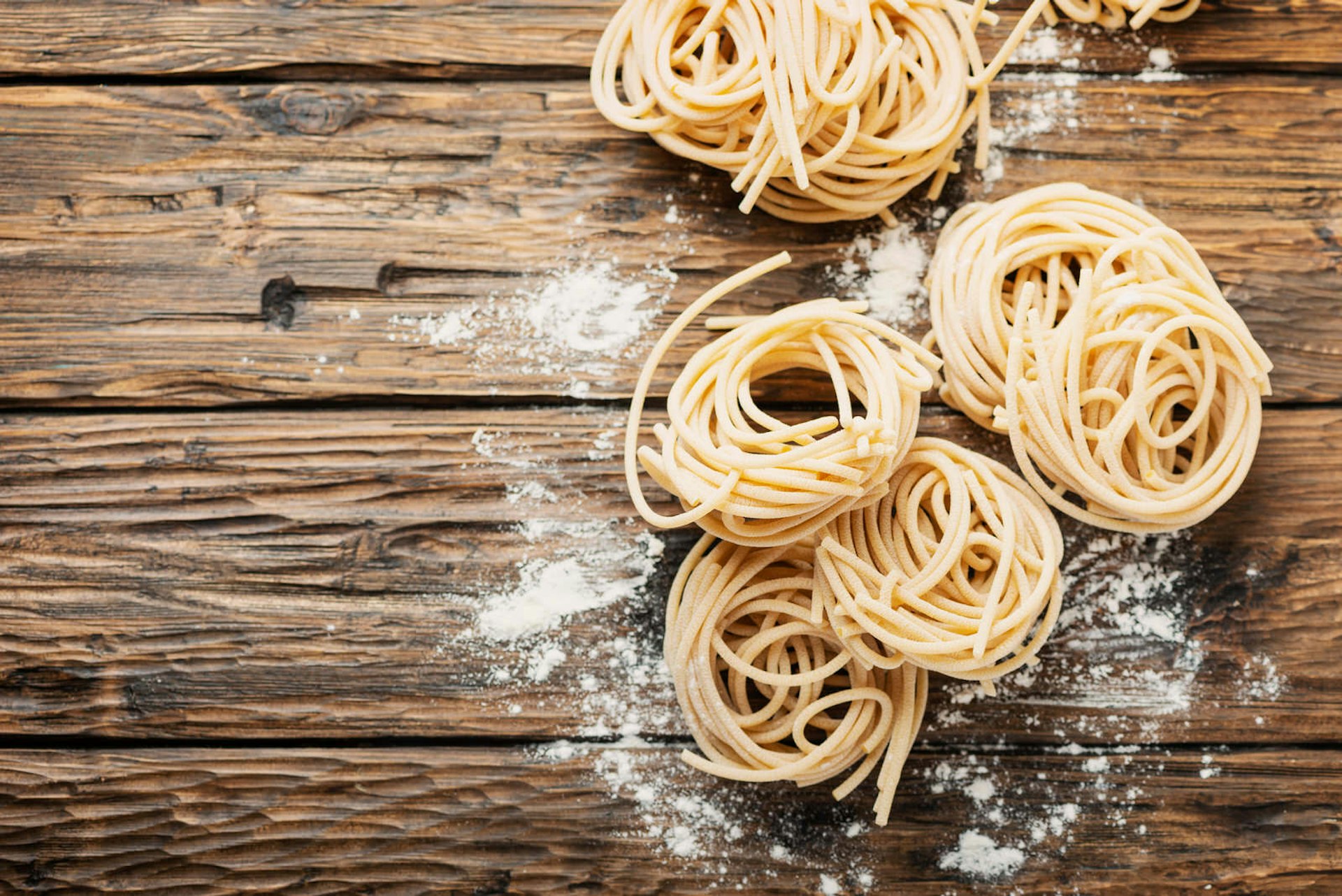 Several uncooked balls of pici pasta from Tuscany on a rough wooden table sprinkled with flour.