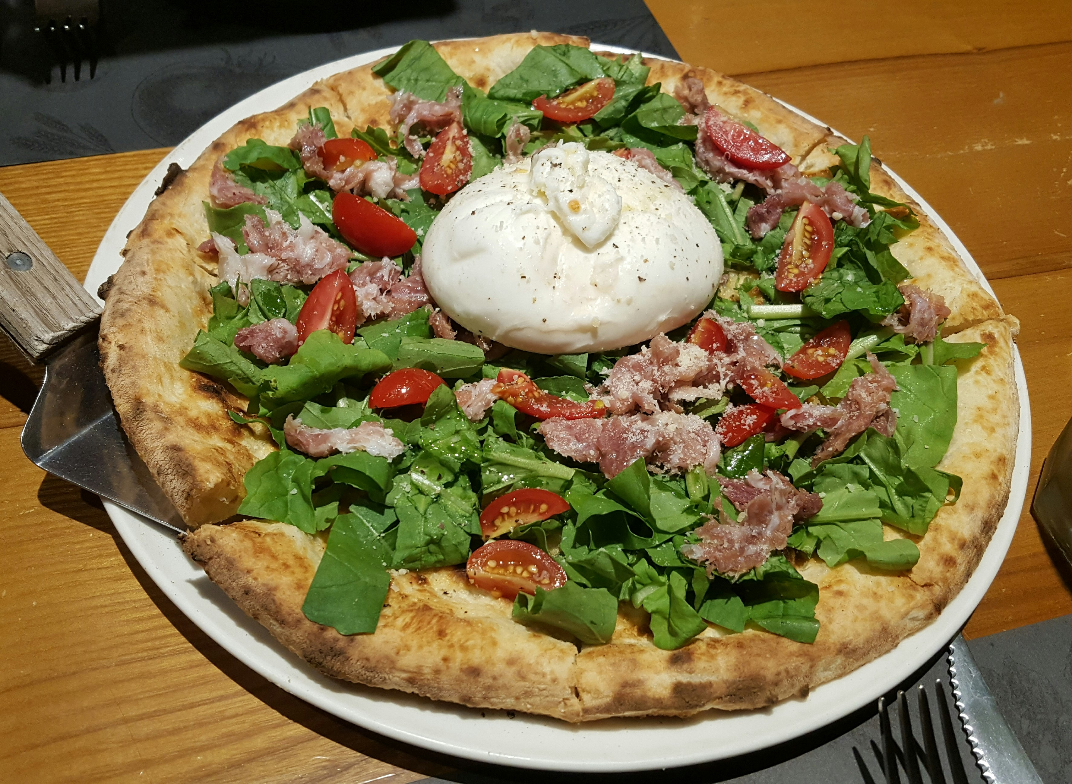 Pizza topped with greens, tomatoes, meat and a poached egg 