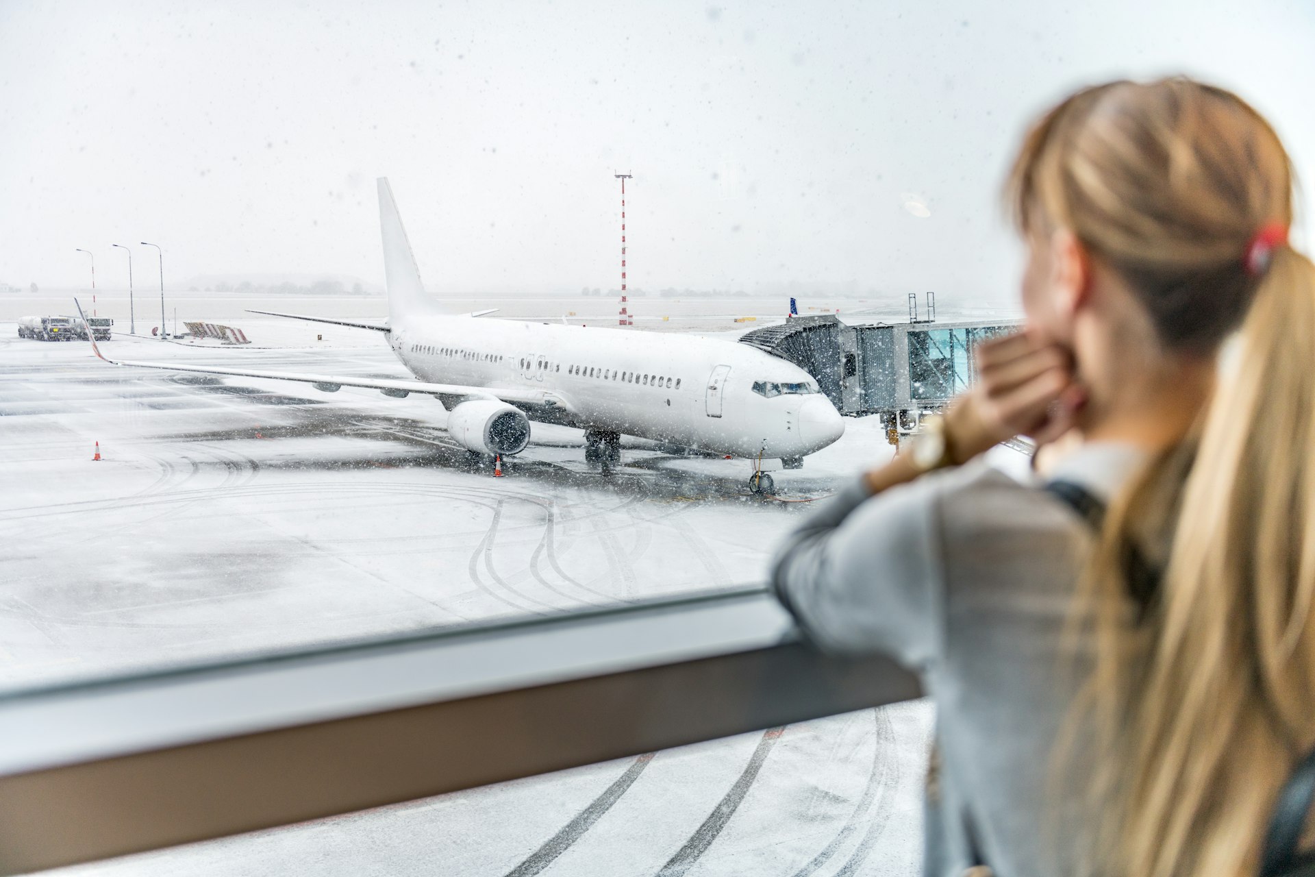 A woman stares on through a window as a plane sits in the snow 