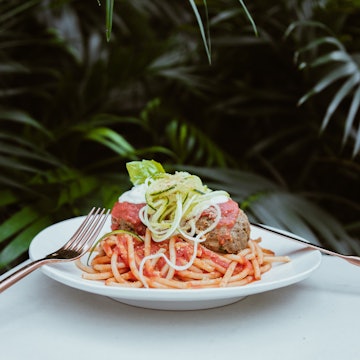 A fork and knife sit on opposite sides of a white plate filled with vegan spaghetti and meatballs; vegan restaurants Miami