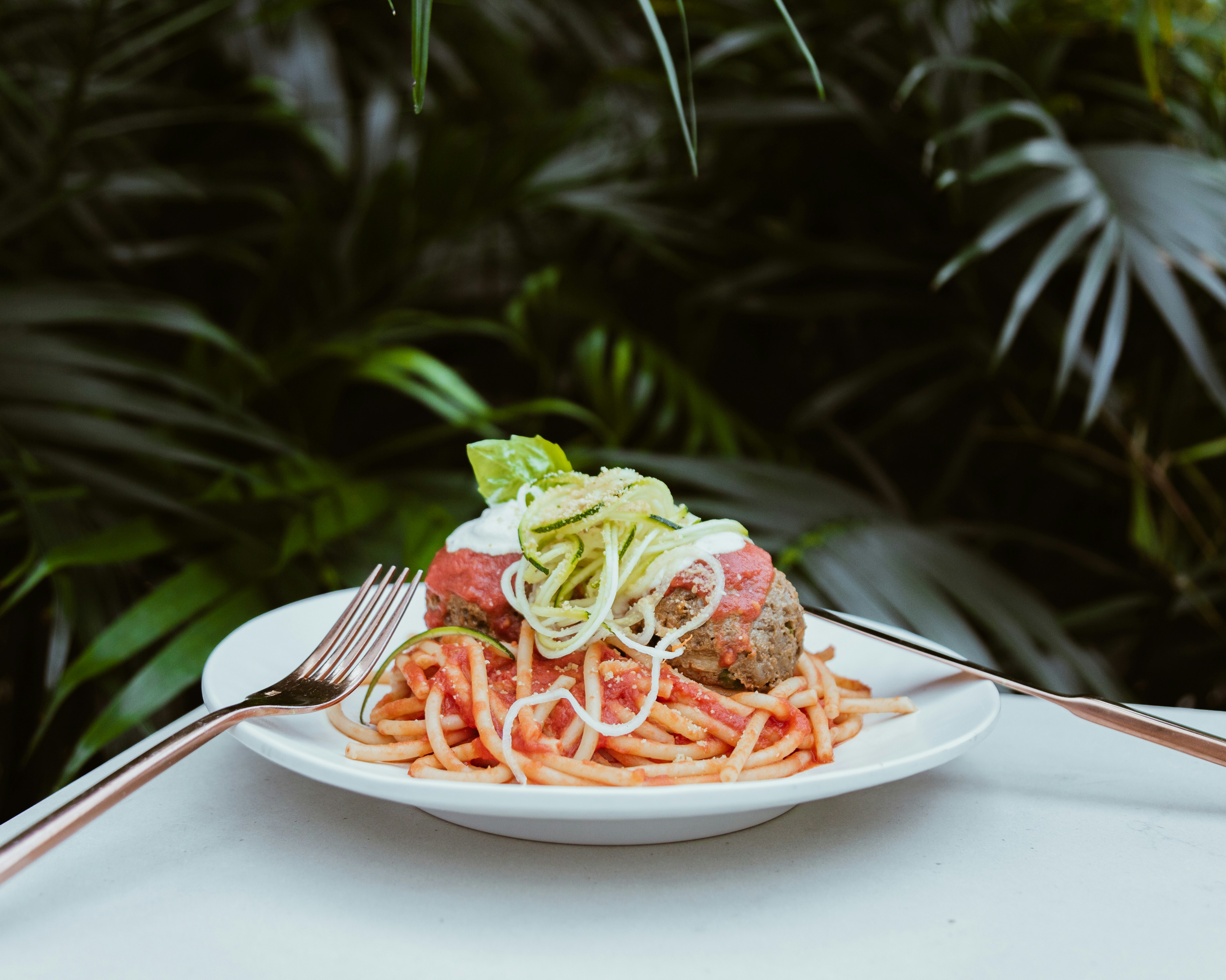 A fork and knife sit on opposite sides of a white plate filled with vegan spaghetti and faux meatballs; vegan restaurants Miami 