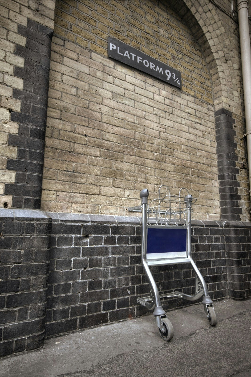 Half of a luggage trolley shows on a brick wall with a sign above that reads Platform 9 3/4