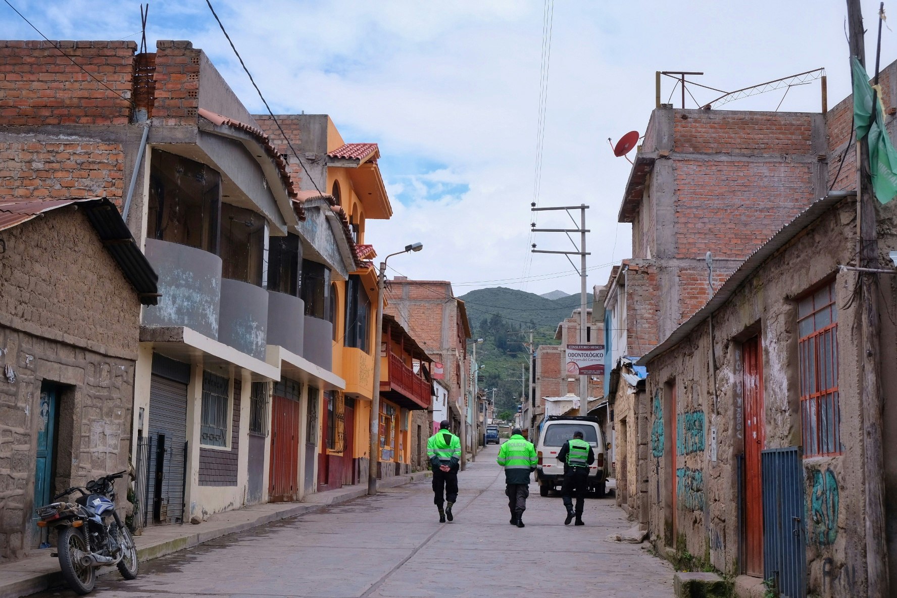 Three police officers in highvis green jackets walk down an empty road in the town of Cabanaconde, Peru.