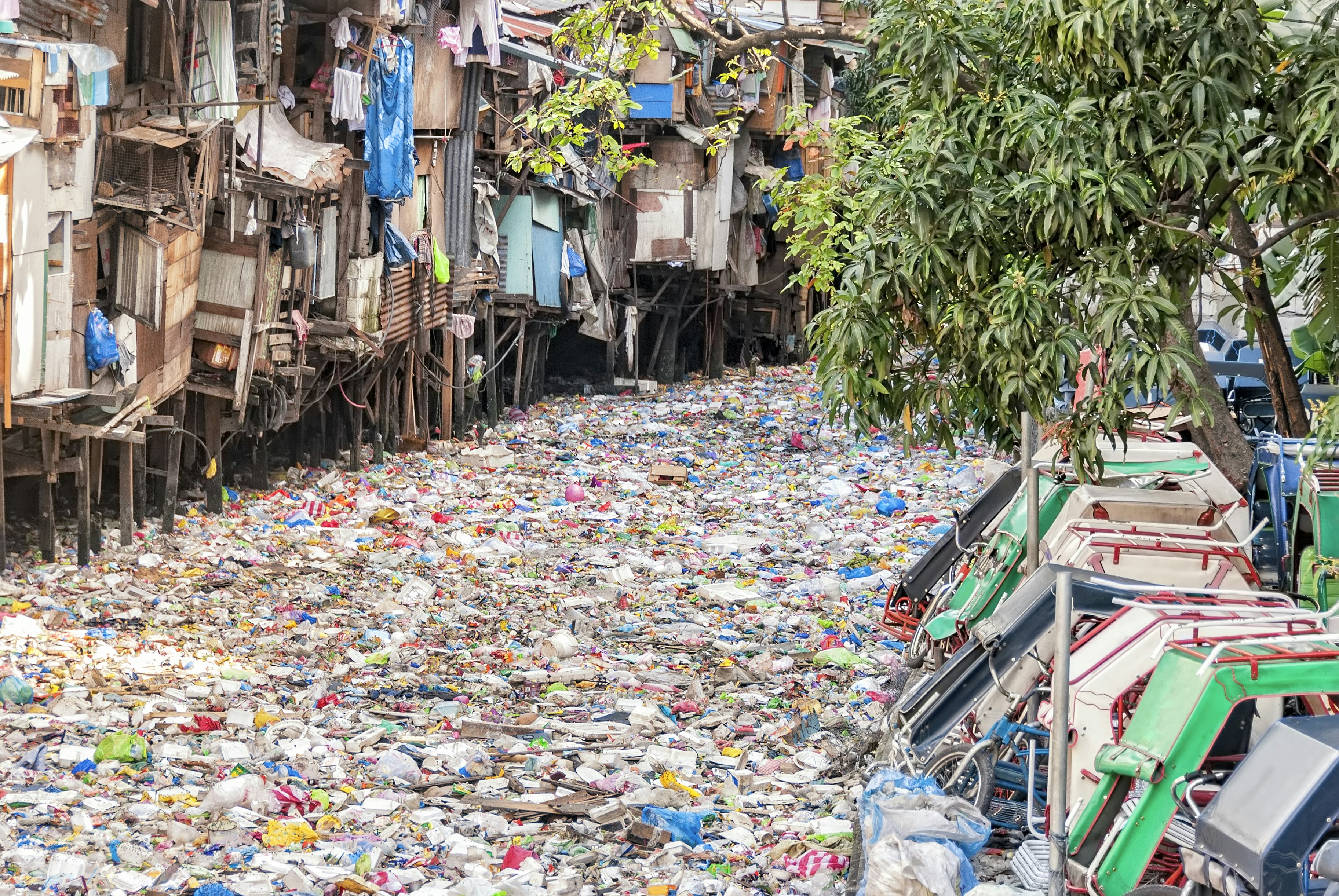 Shanties on stilts standing on garbage-filled river