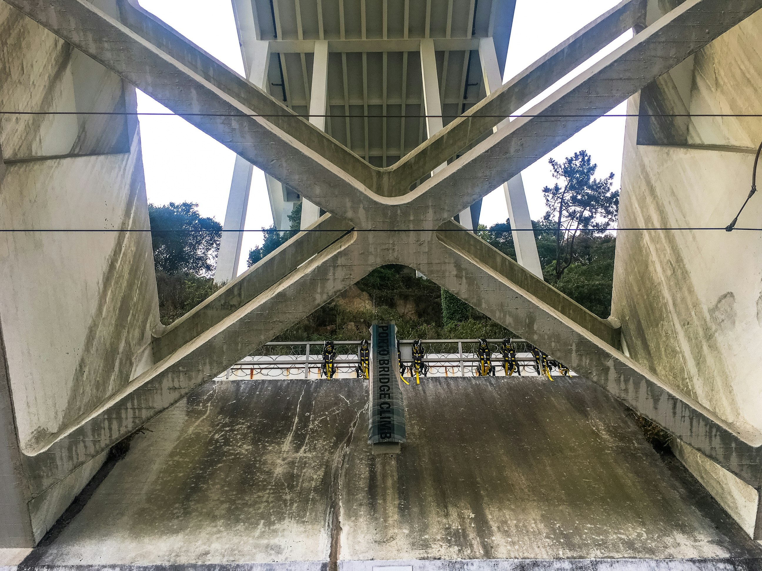 Looking up at the crossed girders of the Dom Luis Bridge towards the start of the Porto Bridge Climb, where yellow and black harnesses are lined up.