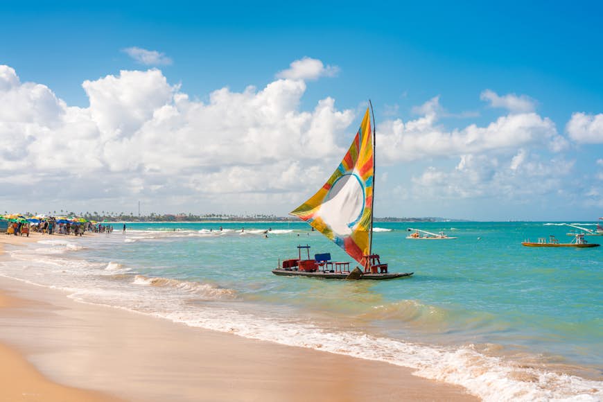 A small boat with a large colorful sail is moored in the shallow waters at Porto de Galinhas, Brazil