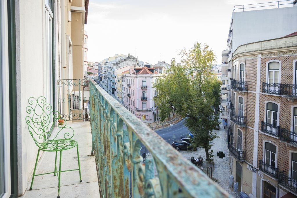 A balcony with an ornate green metal chair, overlooking a colorful street in Lisbon