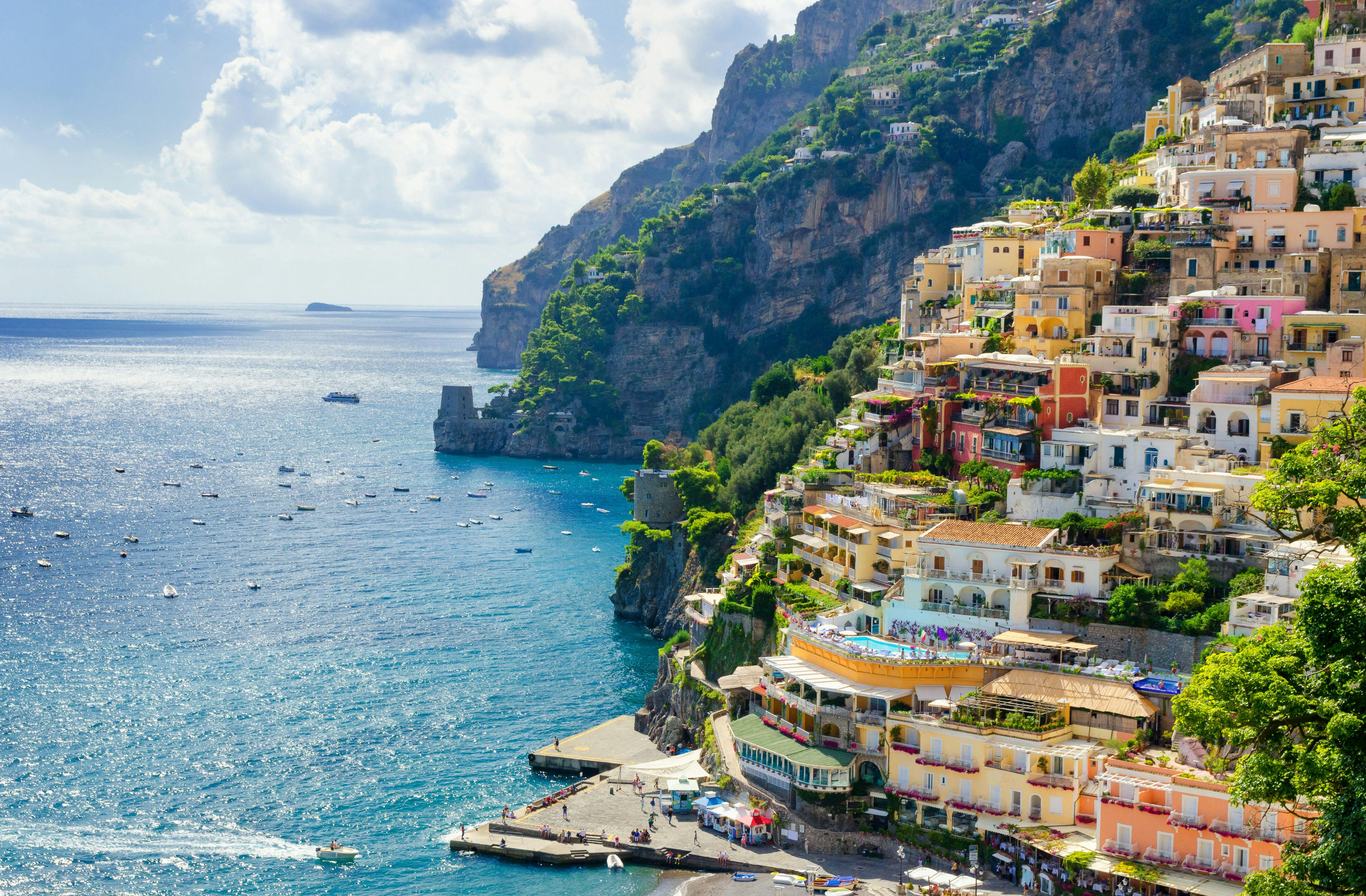 An aerial view of Positano in Italy, with colourful villas built on a sloping hillside that goes right down to the blue waters of the Tyrrhenian Sea.