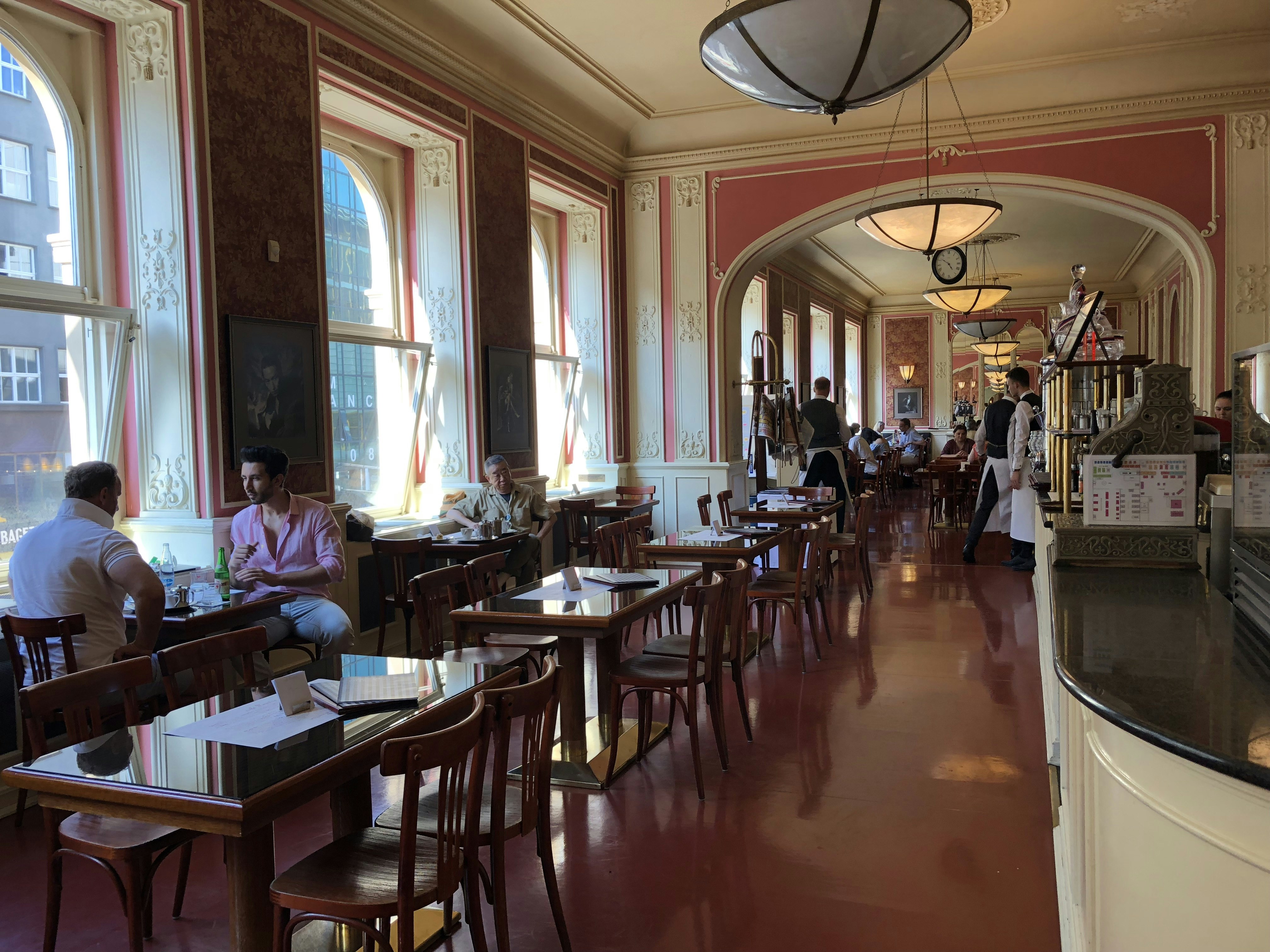 Beskyddare inne i Café Louvre, med högt i tak och blomstrar i parisisk stil