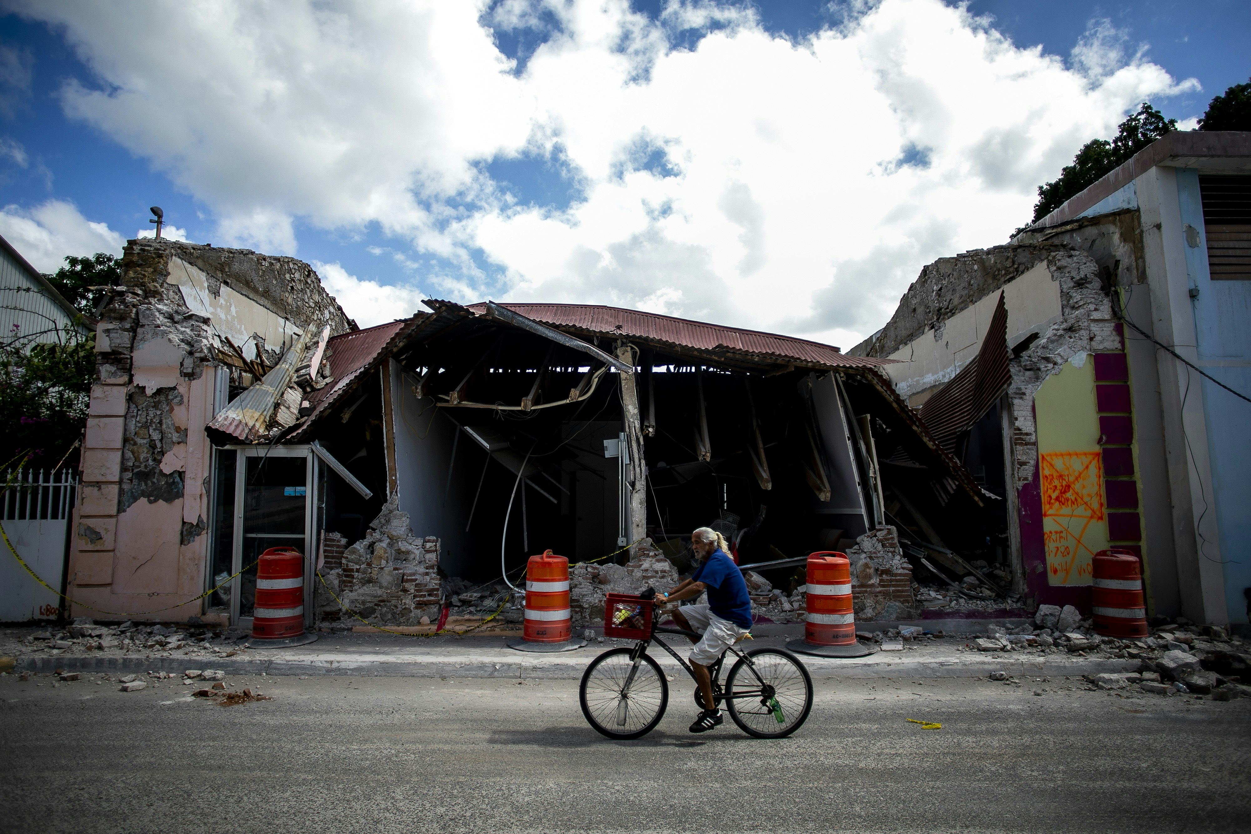 A cyclist rides past a destroyed building in on a street in Guanica, Puerto Rico.