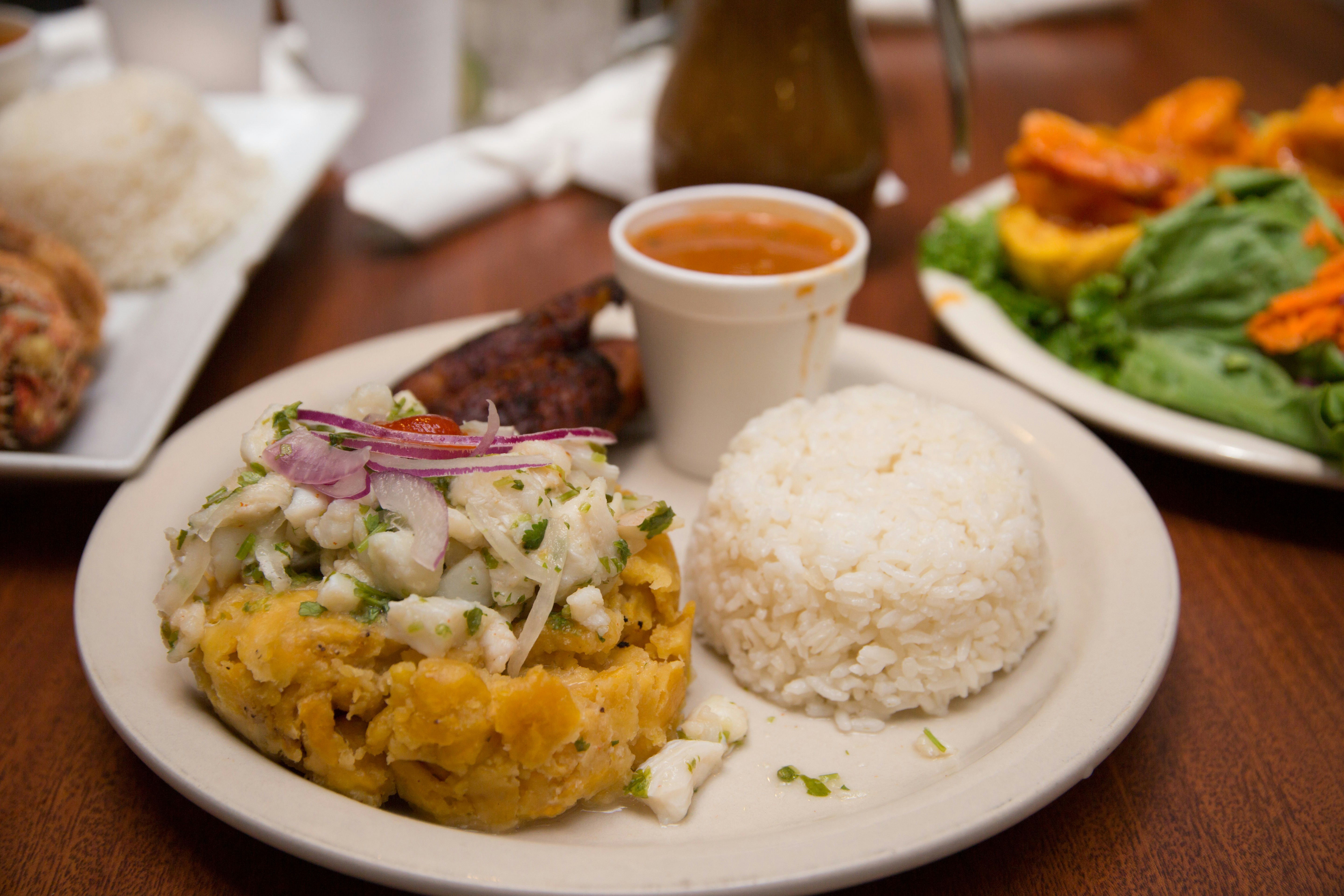 A plate of mofongo, a Puerto Rican dish made of fried plantain topped with meat. The food is on a circular plate resting on a tabletop.