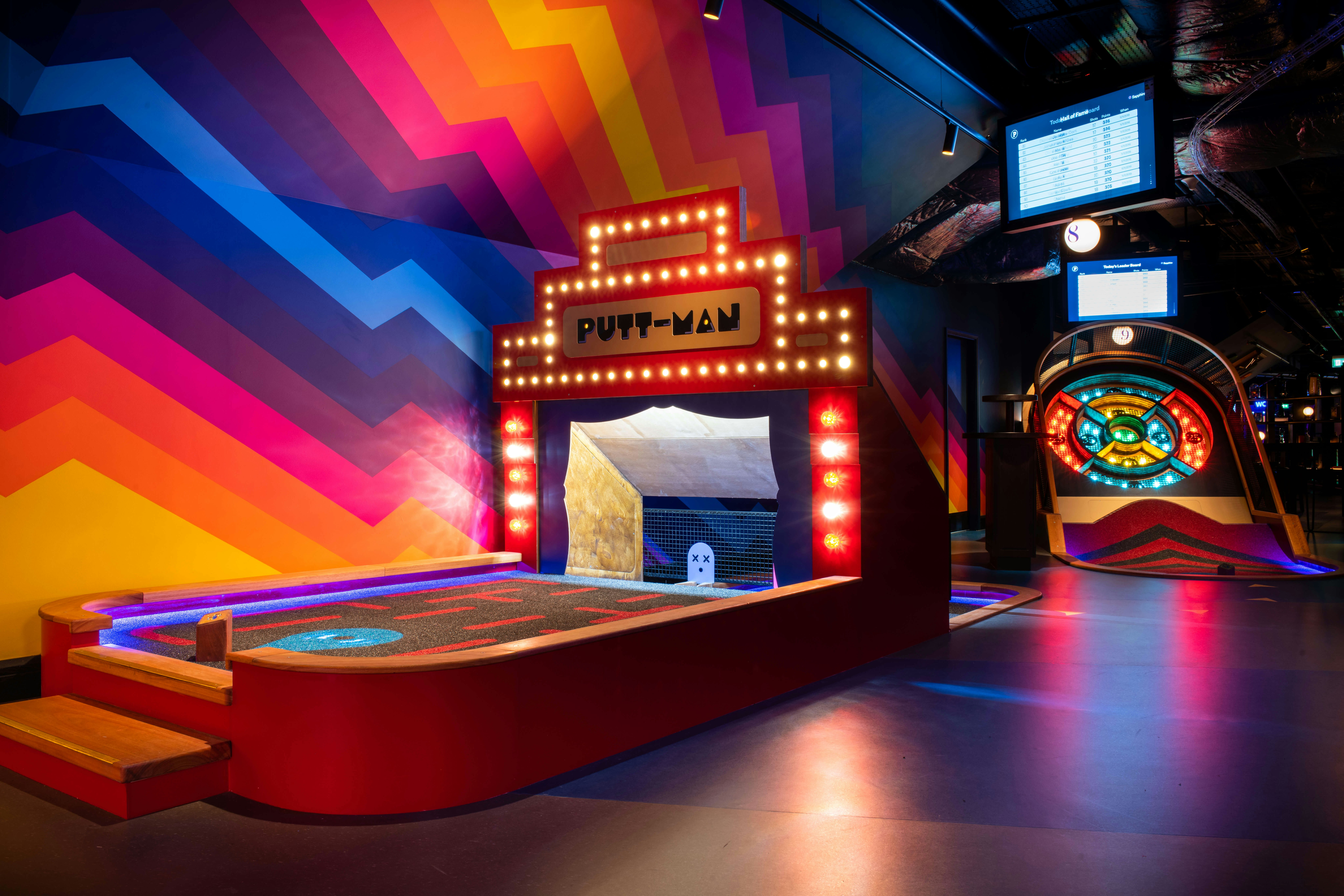 A room painted in bright colors and geometric shapes, with Putt-Man and a light-up skeeball