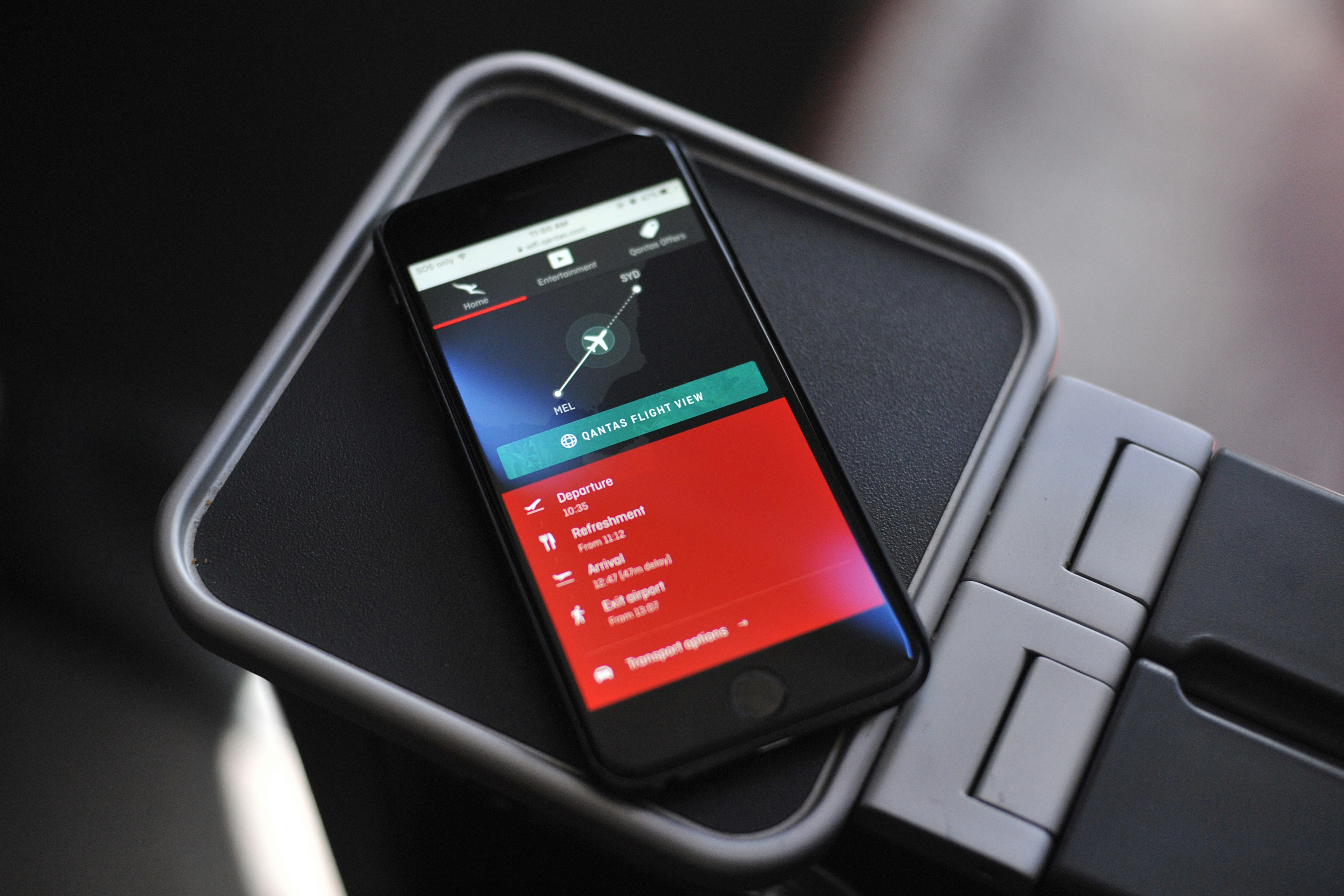 A smartphone showing the Qantas app, sitting on a plane's tray table