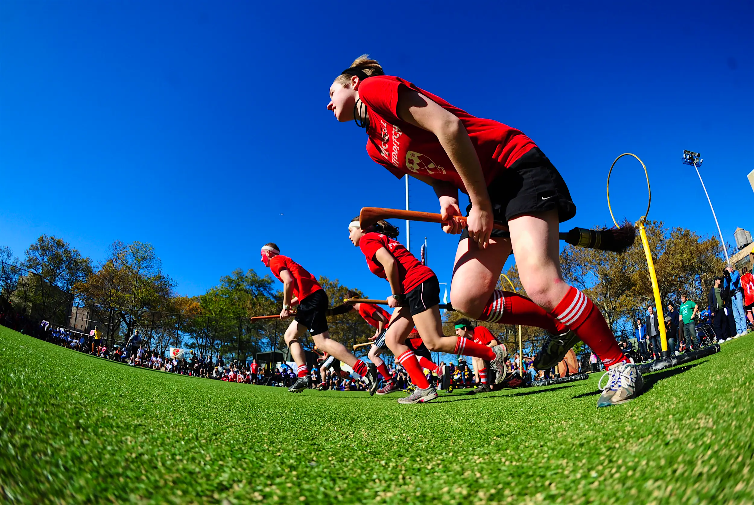 Quidditch.jpg Players in red jerseys run across a field with broomsticks between their legs; Unique sporting events