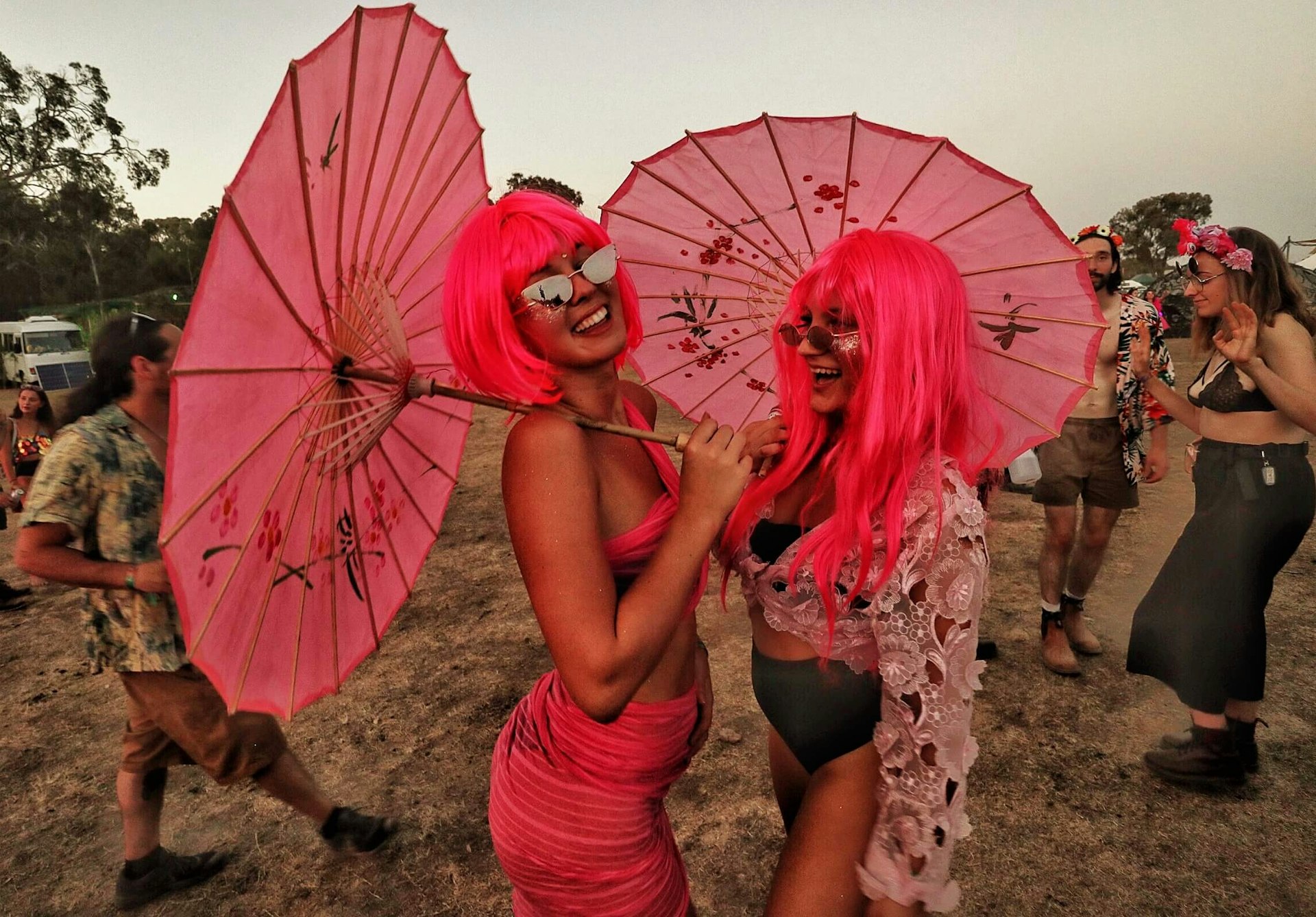 Two women in matching pink wigs and pink-sequined outfits, holding matching pink parasols enjoying Rainbow Serpent Festival