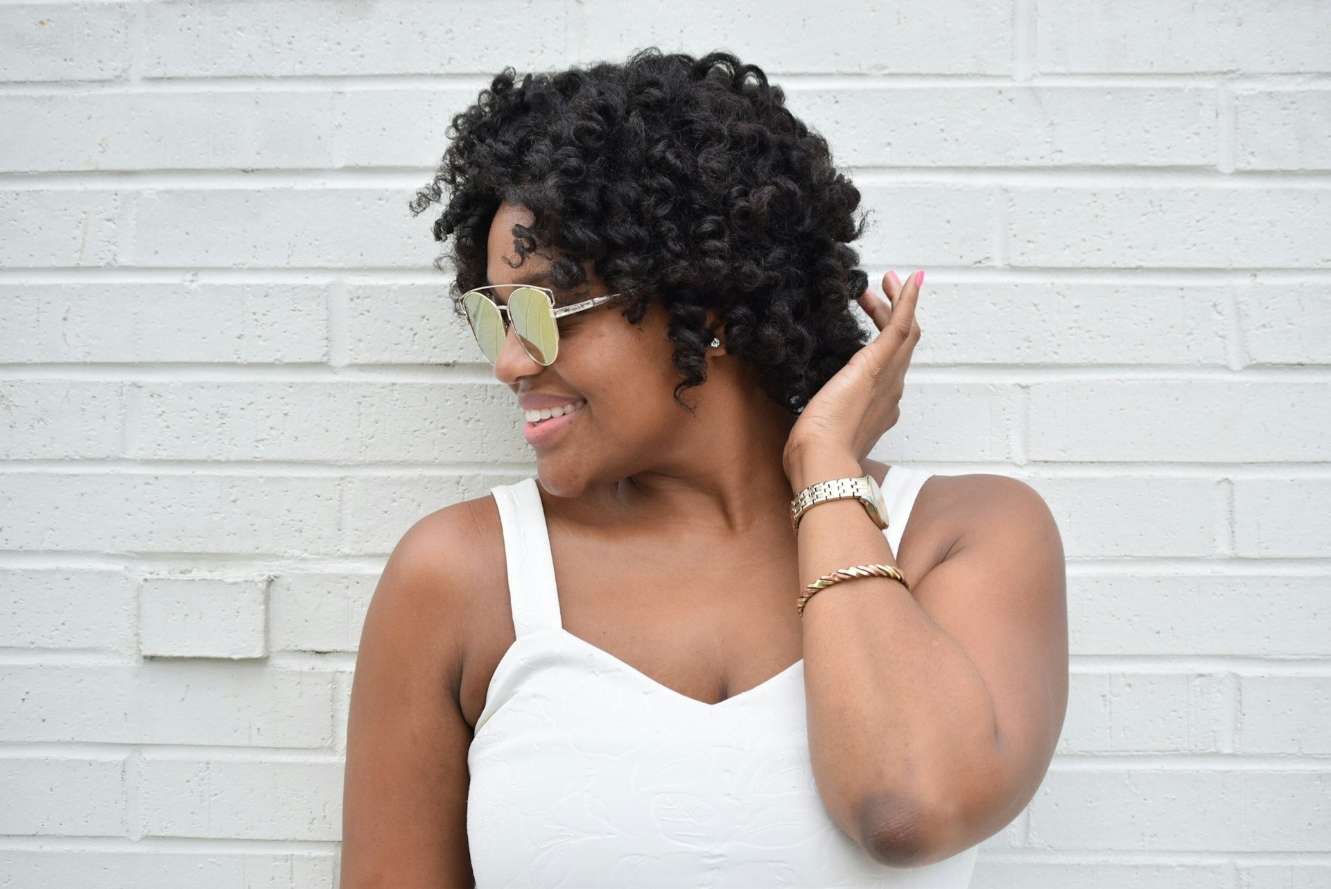 Rachel is standing smiling against a white wall in a white dress with her head turned to the side.