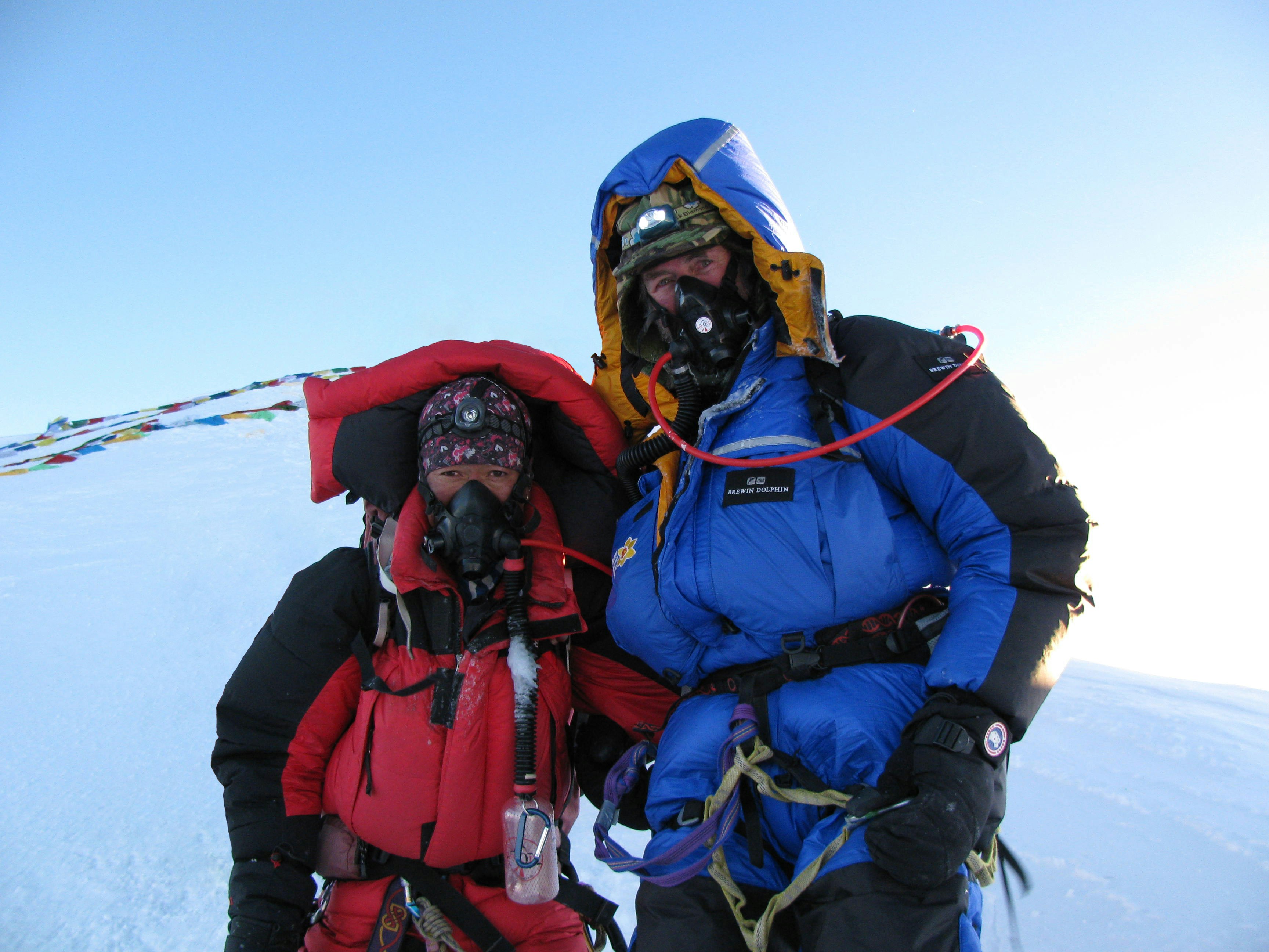 Sir Ran and his short Sherpa guide standing at the summit of Mt Everest; both are wearing oxygen masks and huge down jackets.