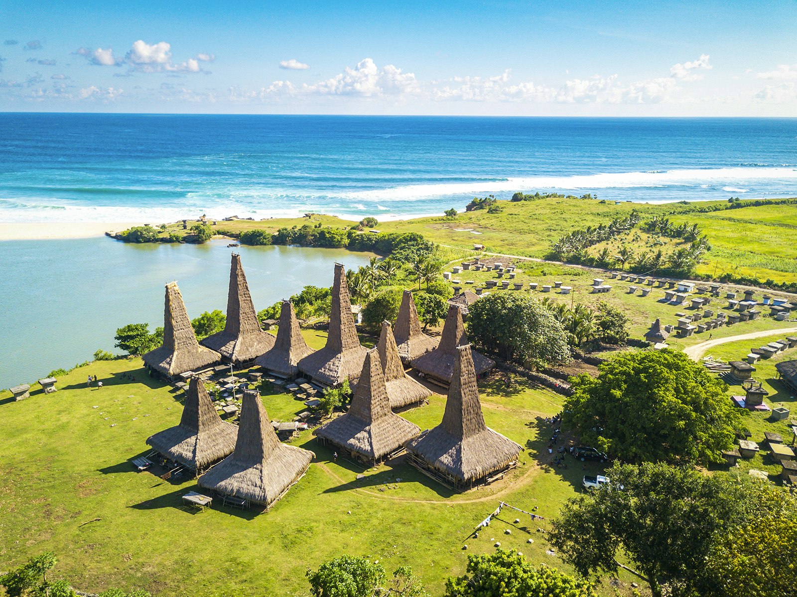 An aerial view of the traditional Indonesian village Ratenggaro; the buildings have pyramid-like roofs, and the community is backed by shoreline. East Nusa Tenggara, Indonesia.